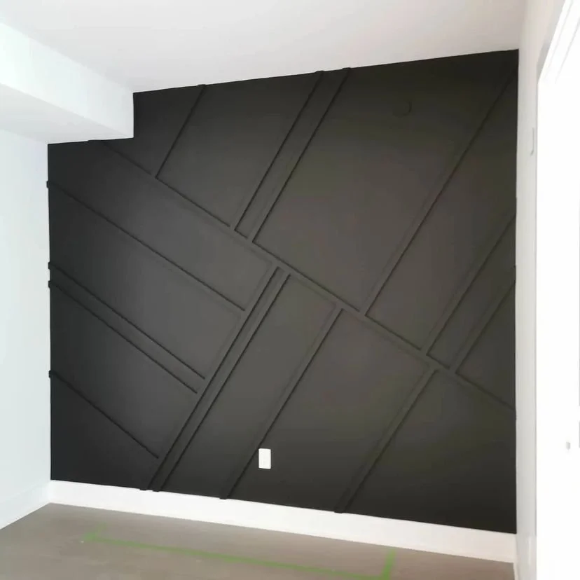 A black accent wall with geometric paneling in a room with white walls and baseboards.