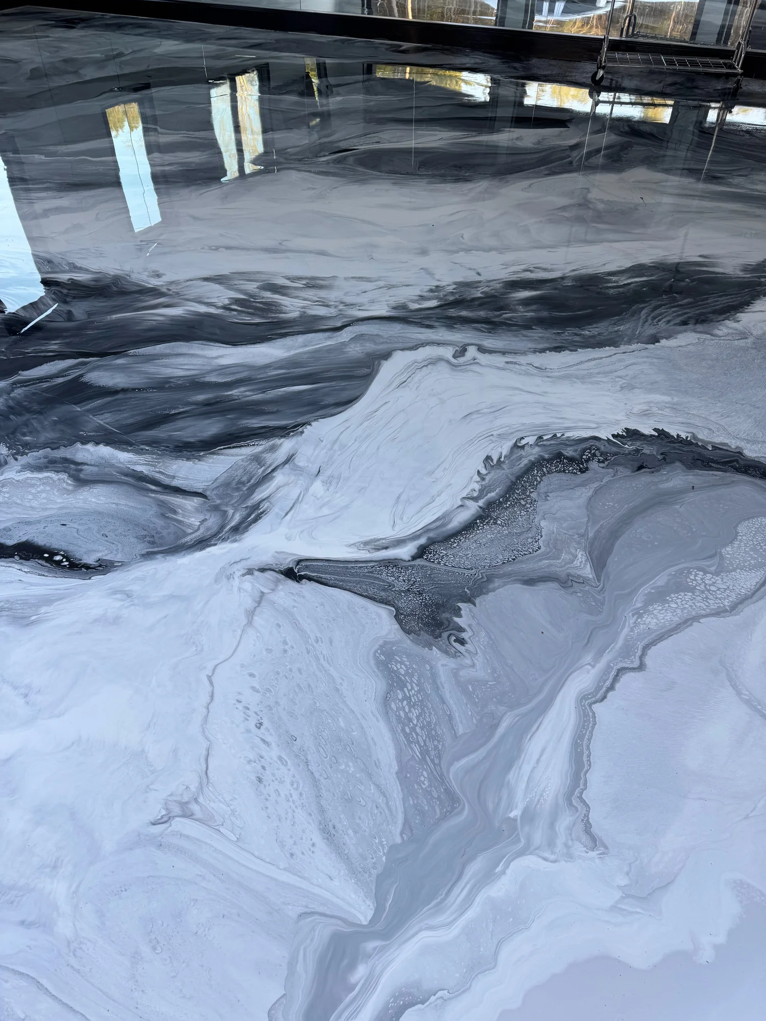 A marble-like surface with swirling black, white, and gray patterns, reflecting windows and part of a metal cart with wheels.