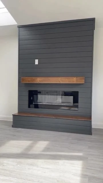 Dark gray shiplap wall with a wooden mantel shelf and a built-in fireplace, in a modern interior setting.