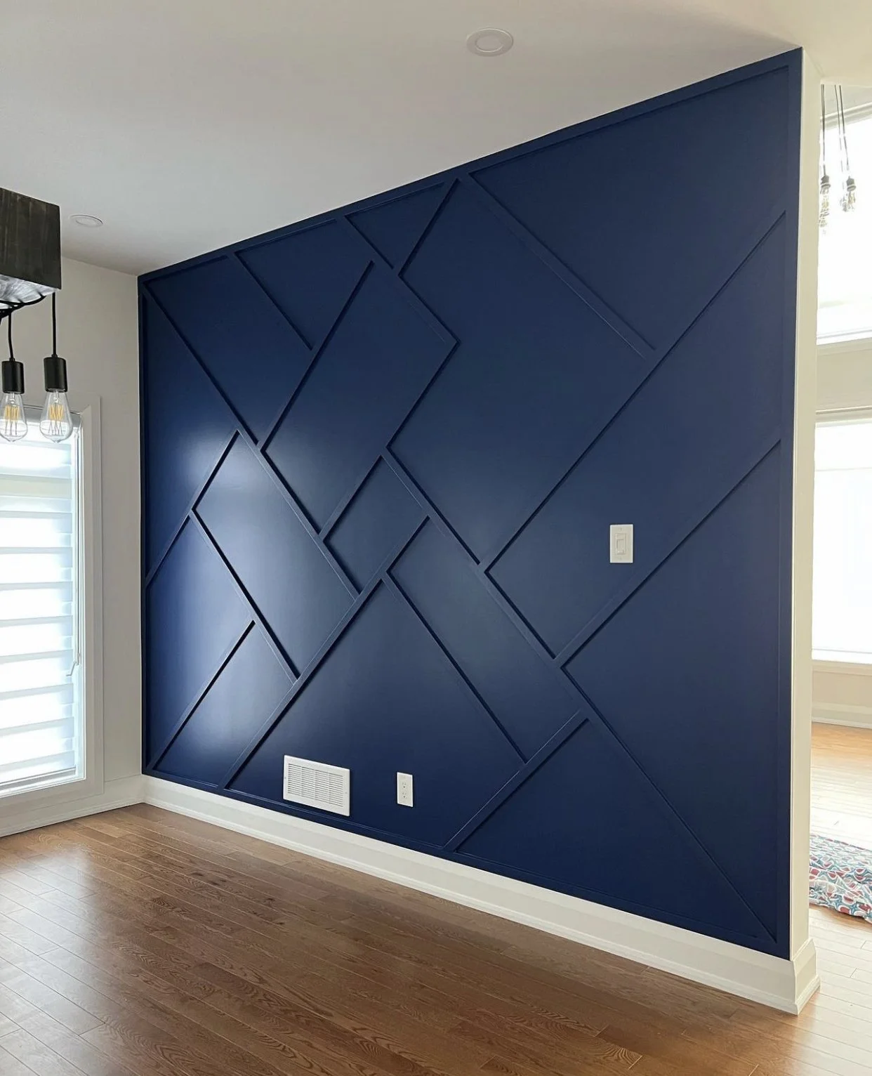 A blue accent wall with a geometric panel design in a room with hardwood floors and a white baseboard.