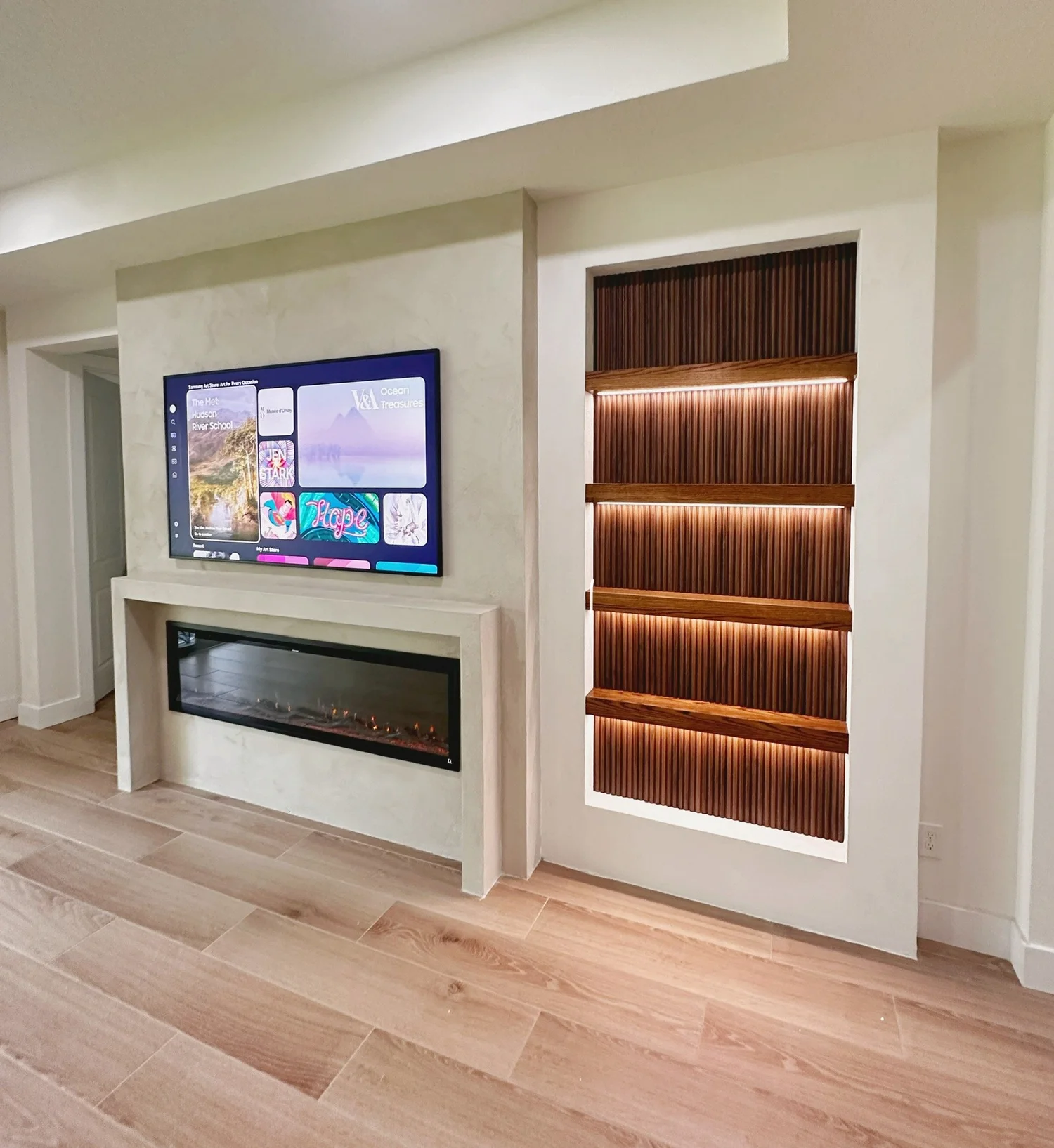 Modern living room fireplace setup with a wall-mounted TV, electric fireplace below, and a decorative wooden panel with backlit shelves on the side.