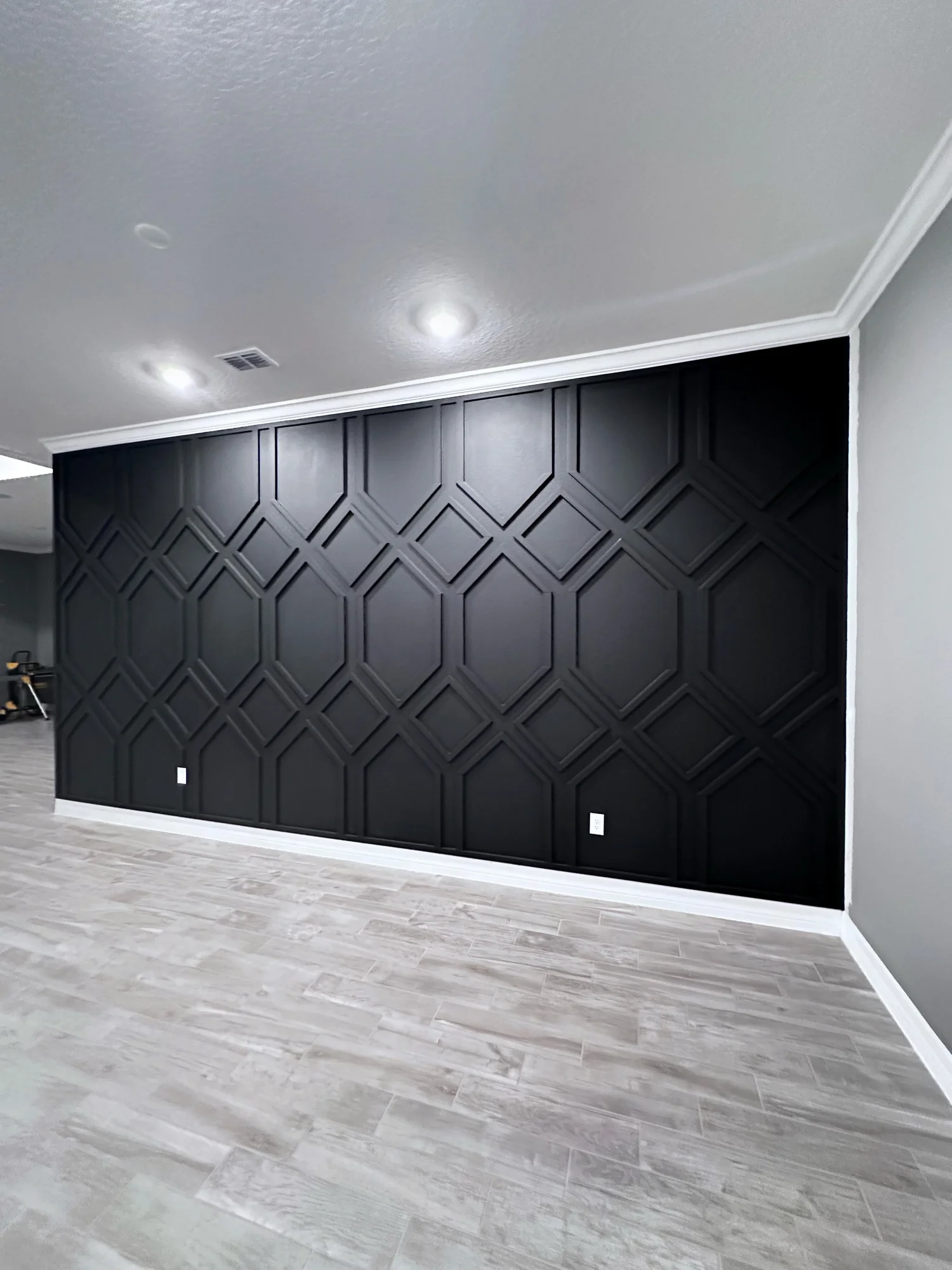 A black accent wall with a geometric pattern in a modern room. The room has light-colored wood flooring and white baseboards.