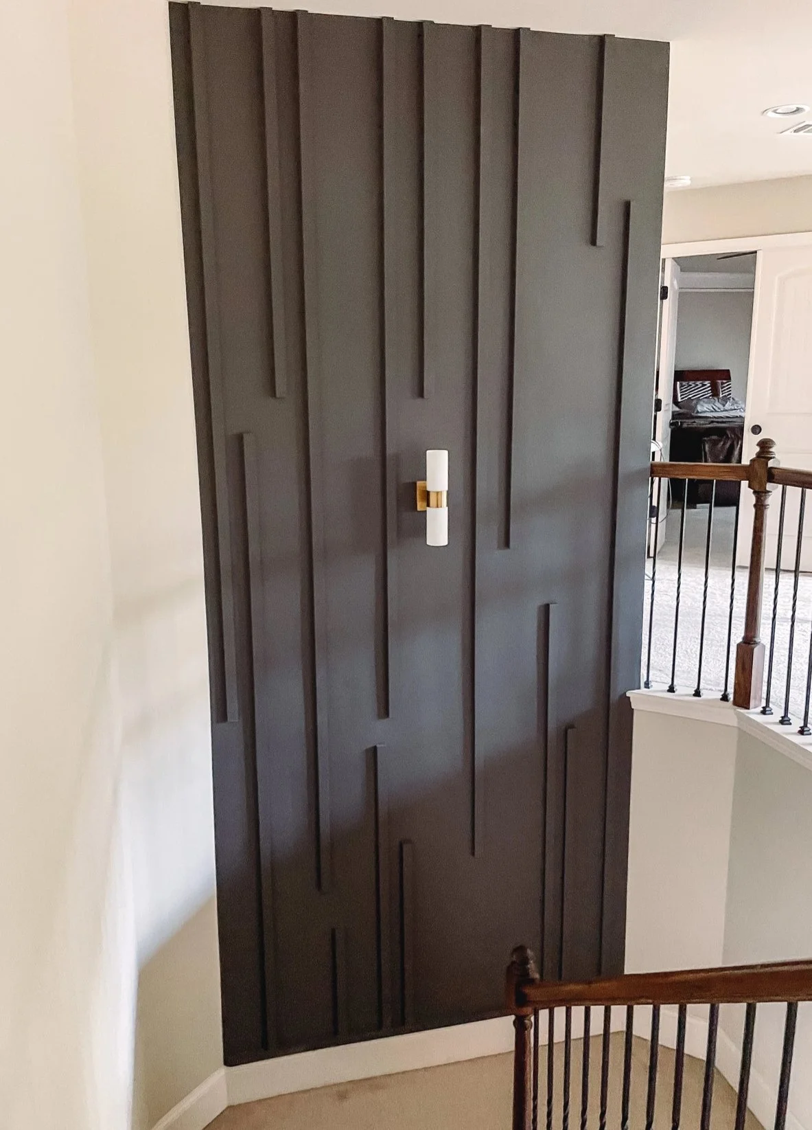 Interior view of a dark brown wooden wall with vertical rectangular design panels, a white wall with shadows, and a light-colored carpeted floor.