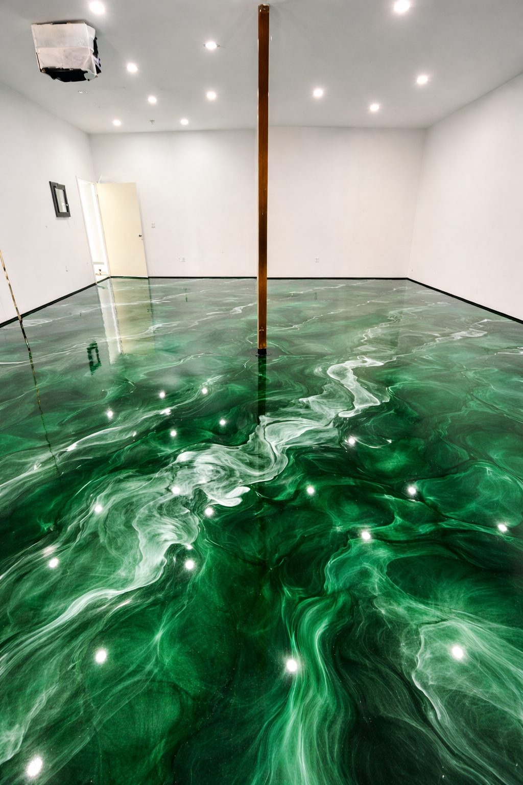 Empty white-walled room with a green, marble-like glossy floor and a wooden pole in the center. Recessed ceiling lights and a wall-mounted TV are visible.
