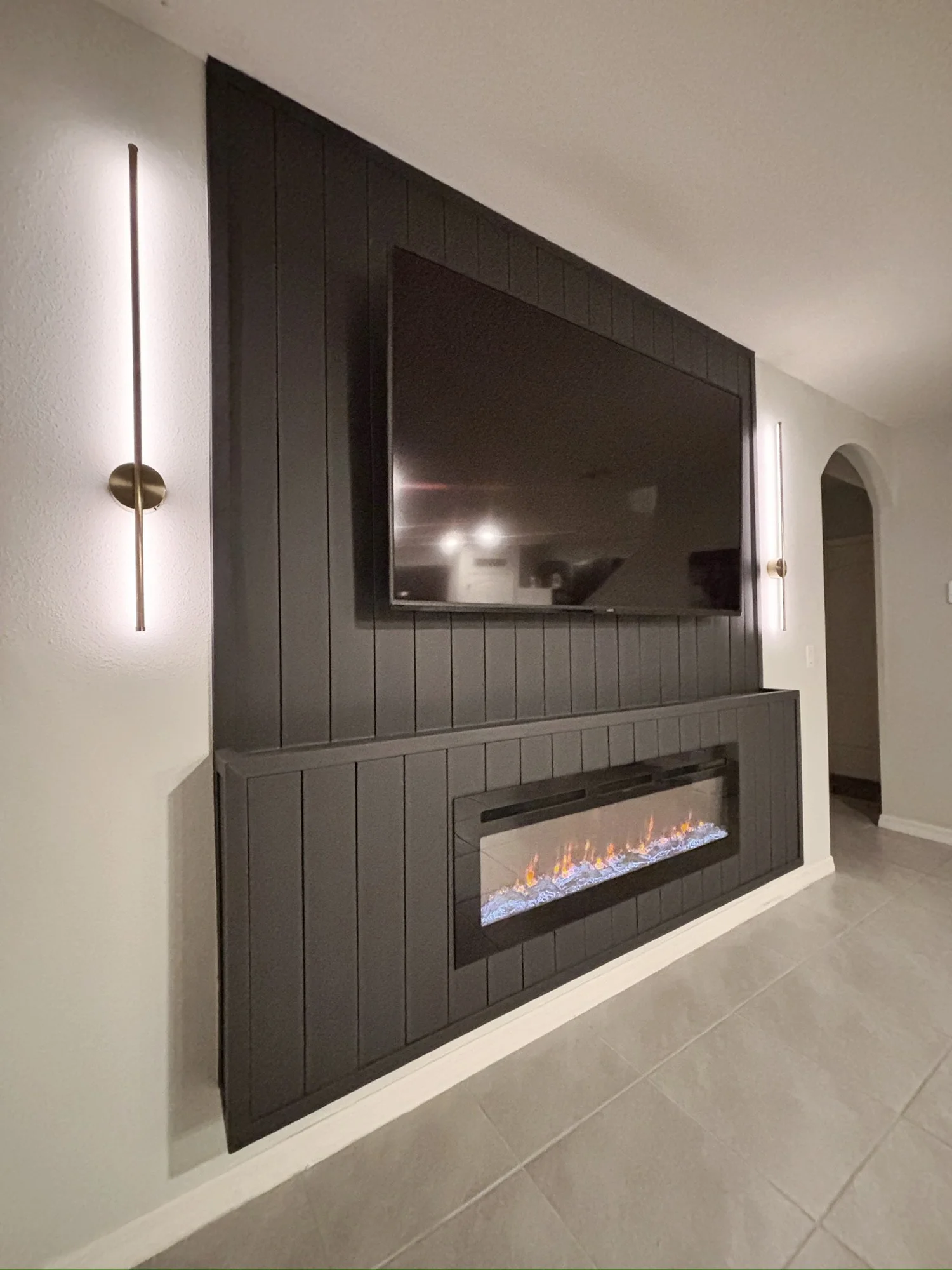 Living room with black paneled wall, mounted flat-screen TV, and built-in electric fireplace with decorative flames.