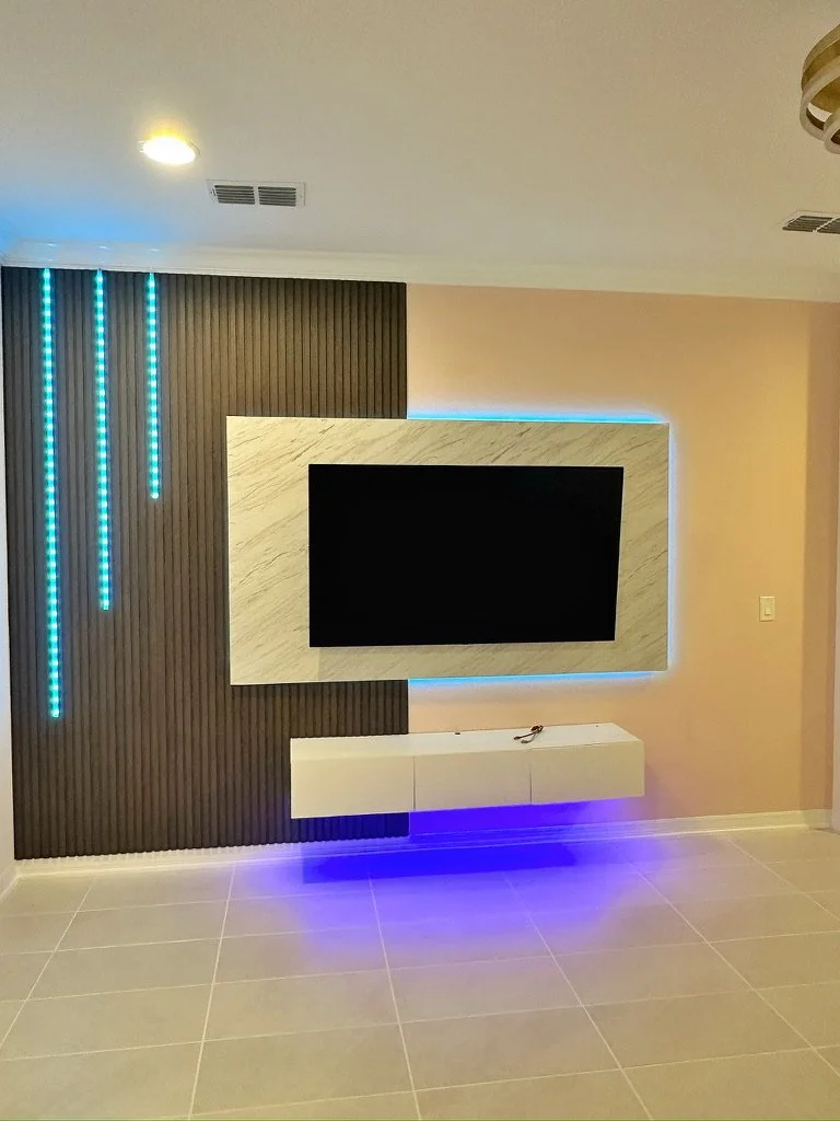 Modern living room wall with a mounted flat-screen TV, illuminated blue LED lighting, and a white wall-mounted entertainment unit.