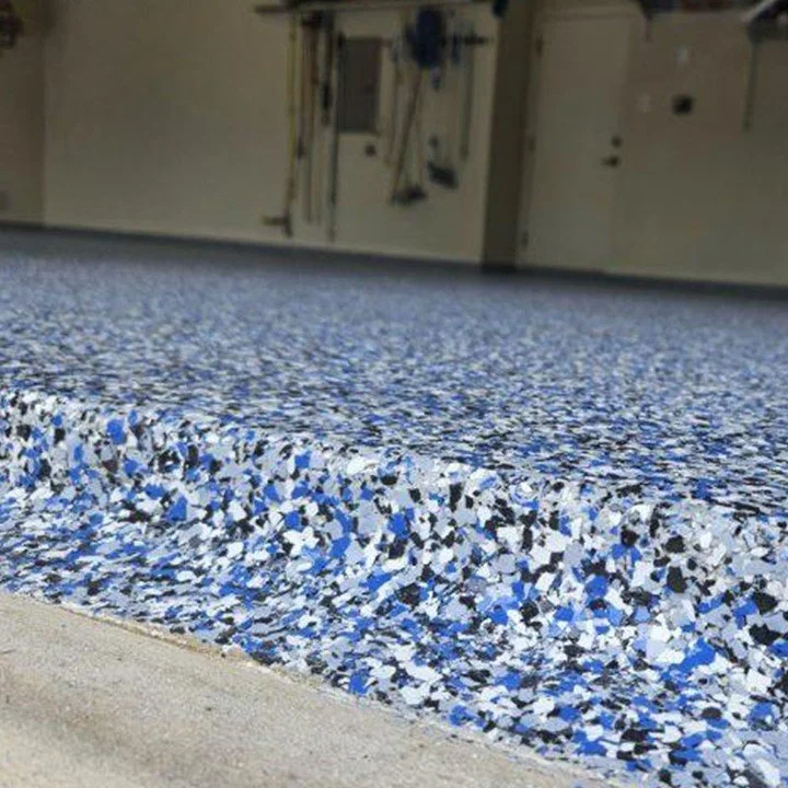 Close-up of textured, blue, gray, white, and black speckled epoxy flooring in a garage with storage cabinets and tools in the background.