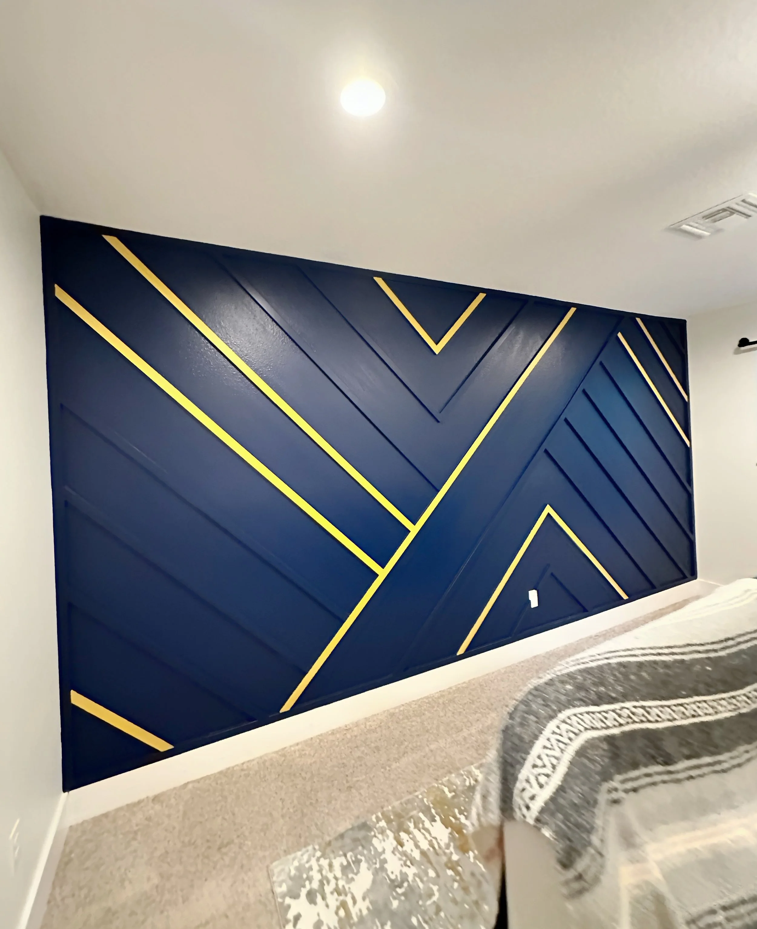 A navy blue wall with gold geometric lines in a modern room, with a beige carpet and partially visible furniture.