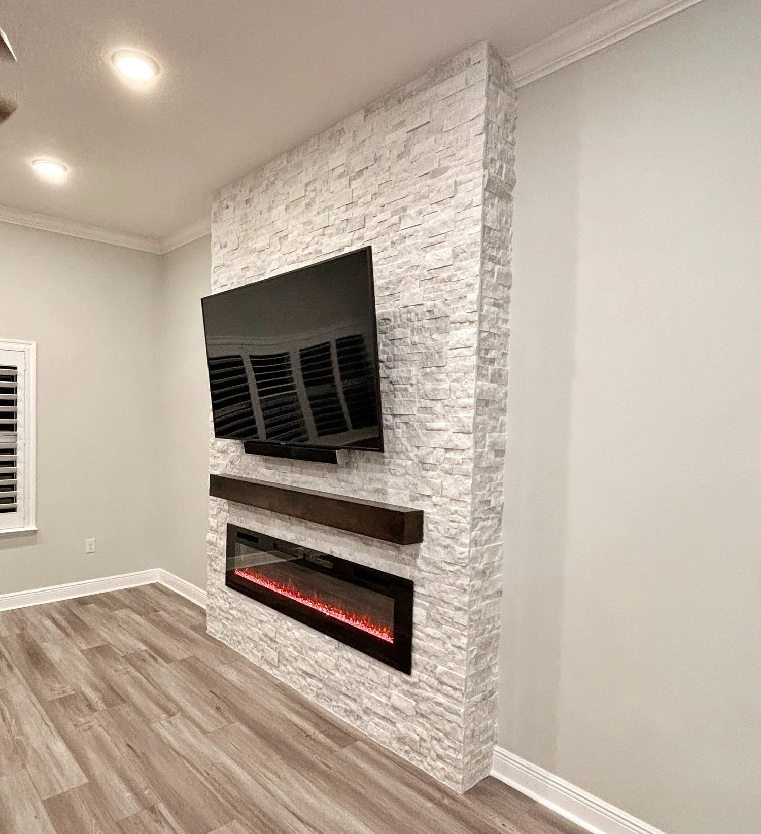 Living room with a wall-mounted flat-screen TV above a modern electric fireplace with a red glowing flame, built into a white stone accent wall.