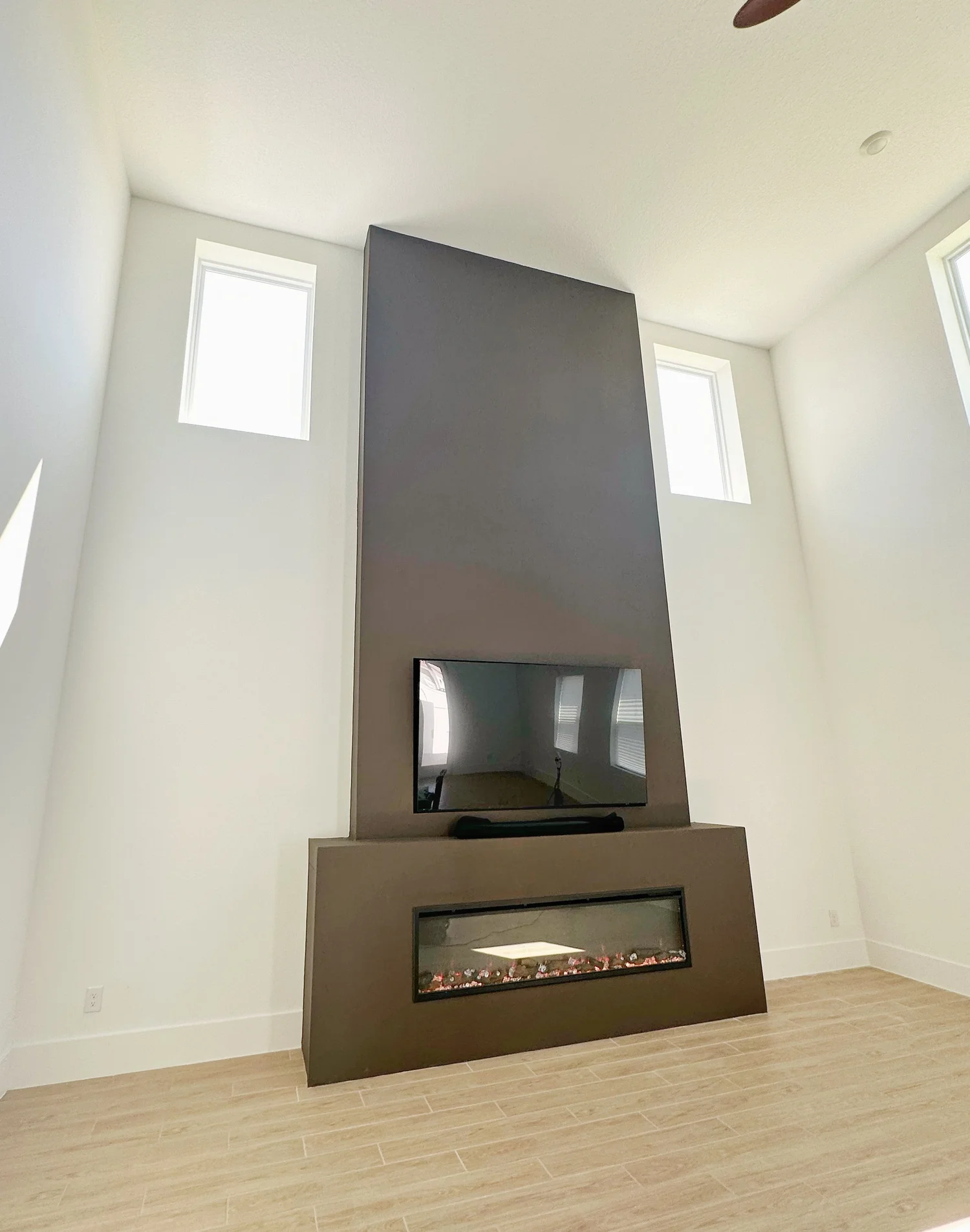 Living room with a mounted flat-screen TV above a modern fireplace in a dark gray wall with white walls and wooden flooring.