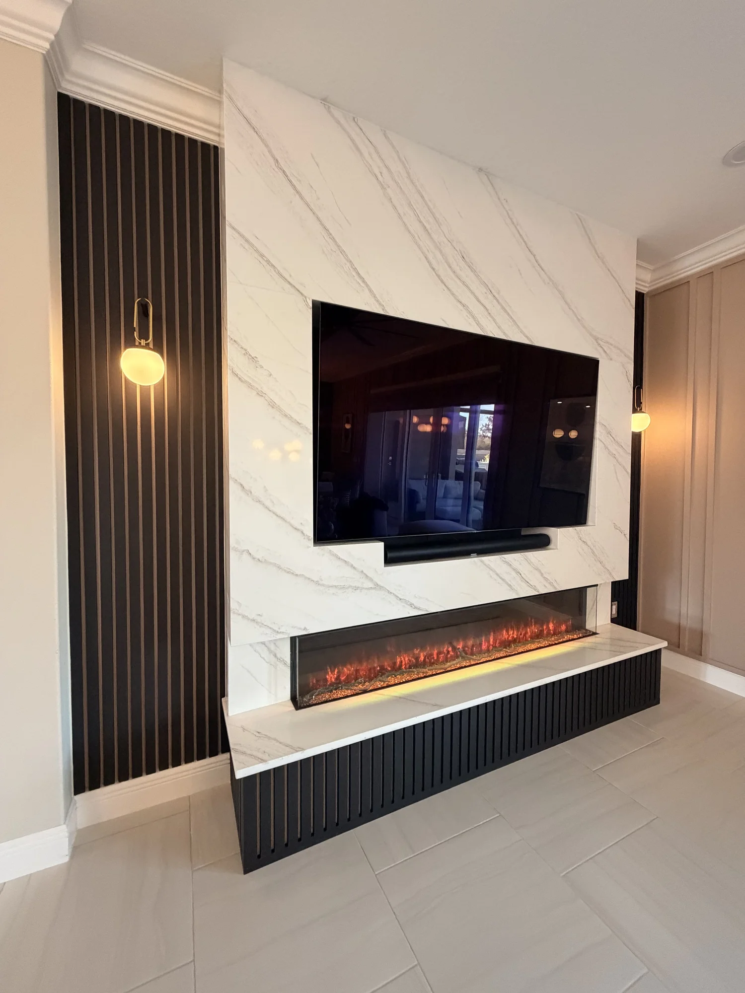 Modern living room wall with a mounted flat-screen TV above a sleek fireplace with glowing embers, flanked by black slatted wooden panels and a marble accent wall.