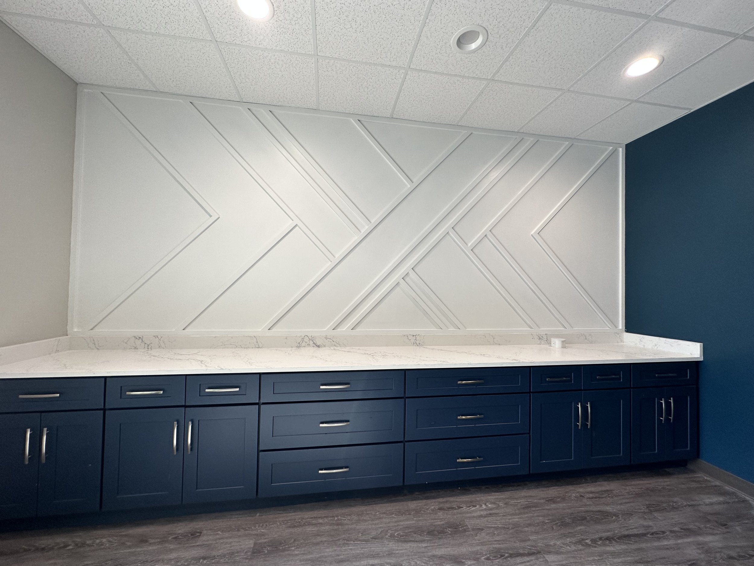 Modern kitchen cabinetry with navy blue lower cabinets and a white marble countertop, featuring a geometric white textured wall design and a blue accent wall.
