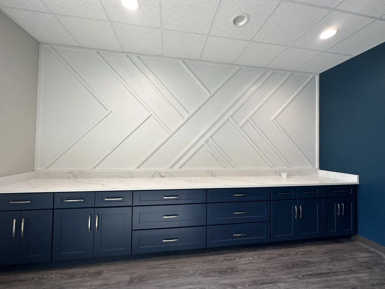 Modern kitchen cabinetry with navy blue lower cabinets and a white marble countertop, featuring a geometric white textured wall design and a blue accent wall.