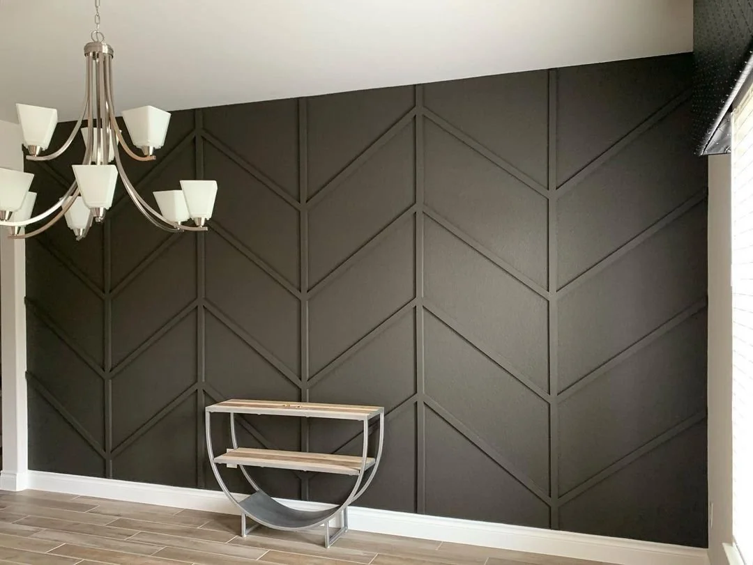 Interior corner of a room with geometric dark wall paneling, a modern chandelier, and a small glass table with wooden shelves.