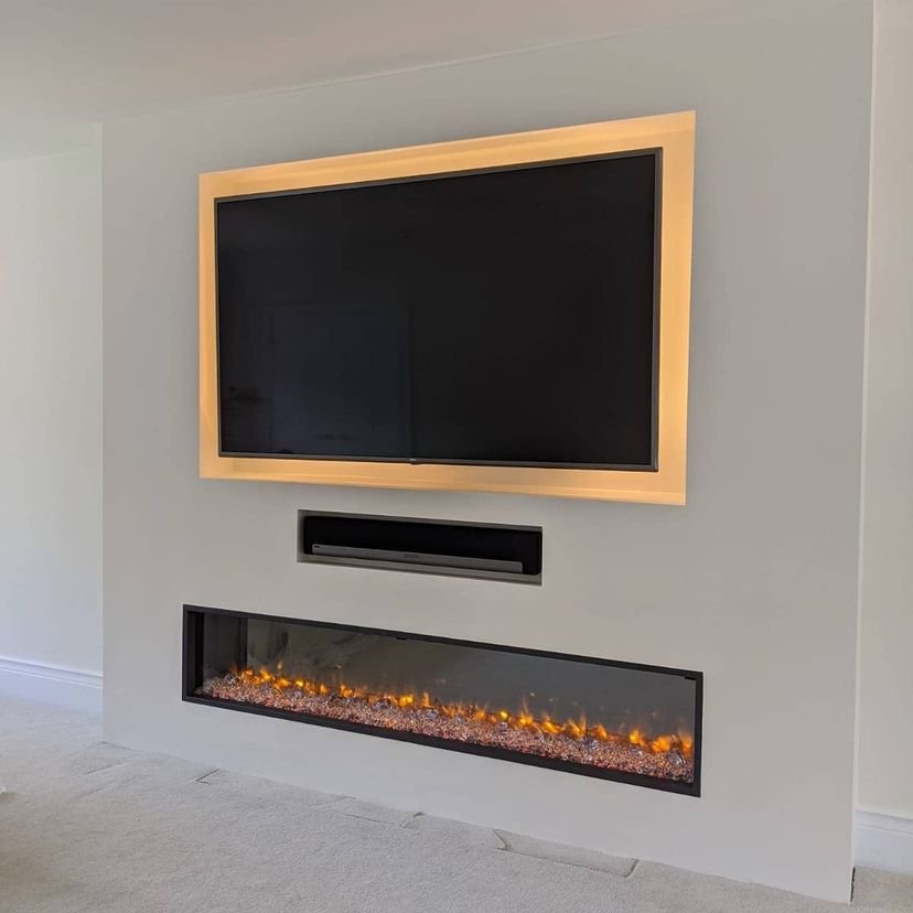 Mounted flat-screen television with a frame, an electric fireplace below it with glowing flames and decorative stones, and a soundbar in between.