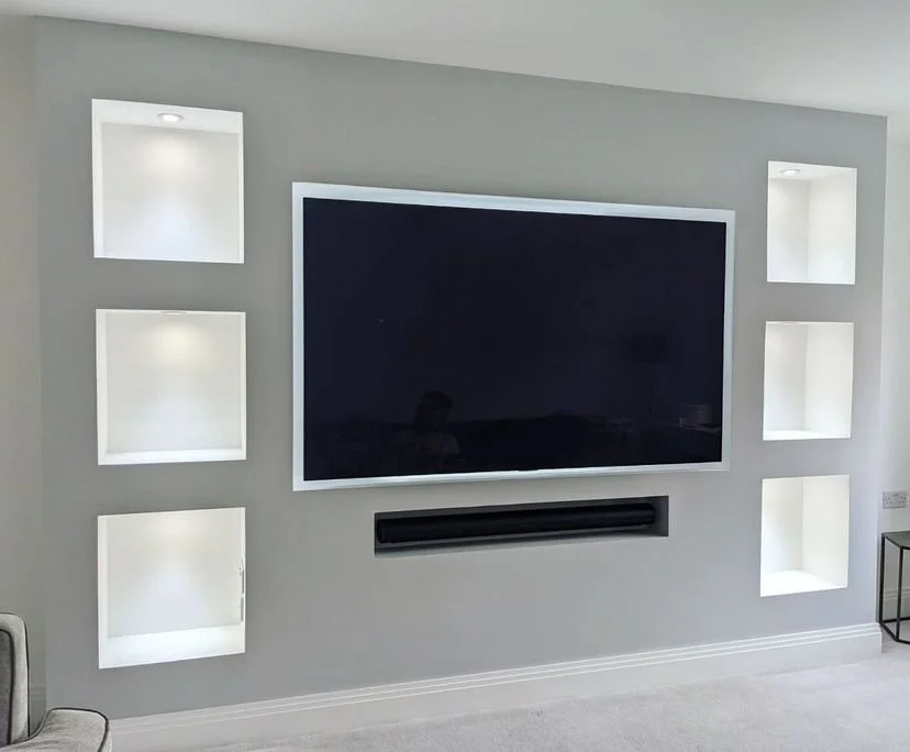 Living room wall featuring a flat-screen TV and four illuminated built-in wall niches, two on each side of the TV.