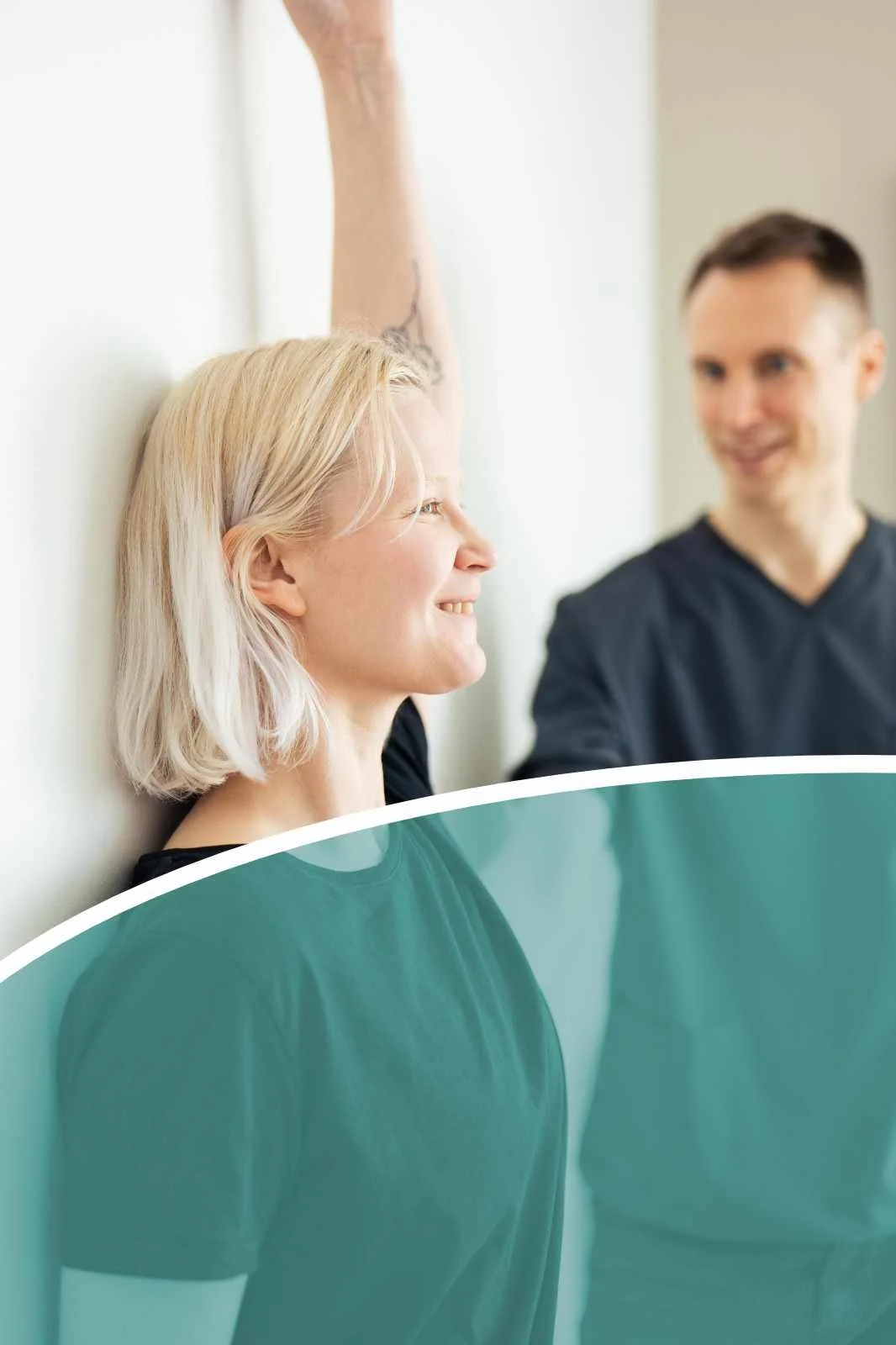 A woman with blonde hair smiling and leaning against a wall, raising her arm. A man sitting nearby is smiling at her. There is a green curved shape in the foreground.