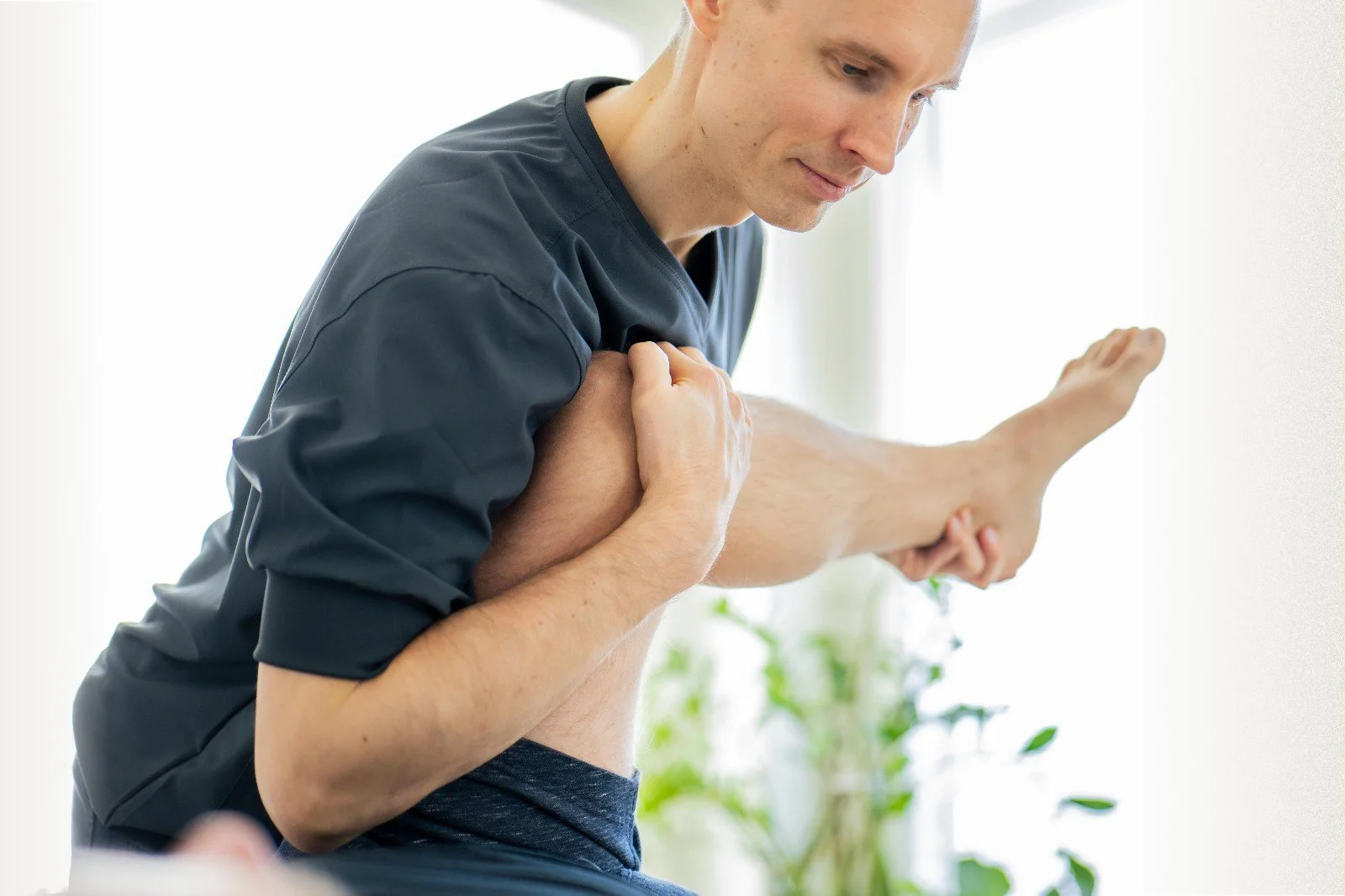 Physical therapist helping a young man stretch his leg in a therapy session.