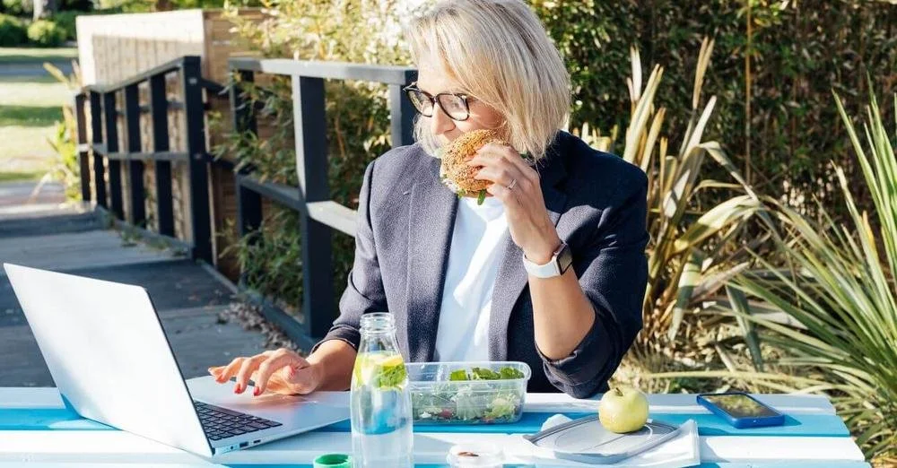 blong woman at outdoor desk looking at laptop with plants and blues in tablecloth