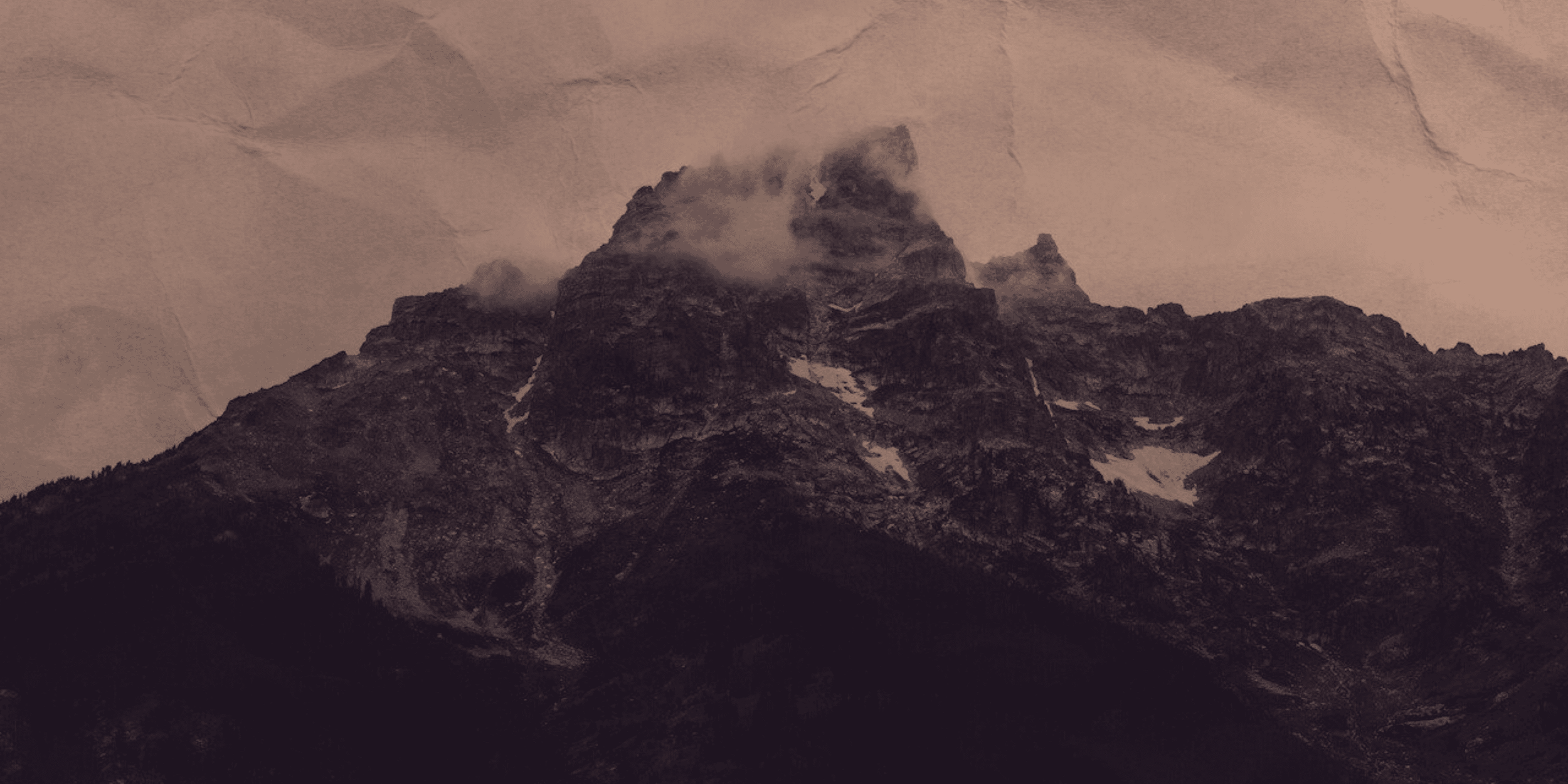 A mountain with multiple peaks partly covered by clouds, with snow patches on the rocky slopes.