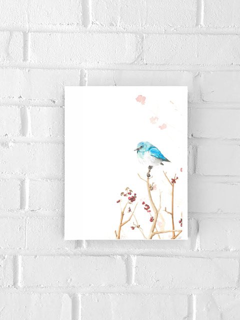 Watercolor painting of a blue bird perched on a branch with red berries, on white background, hanging on a white brick wall.