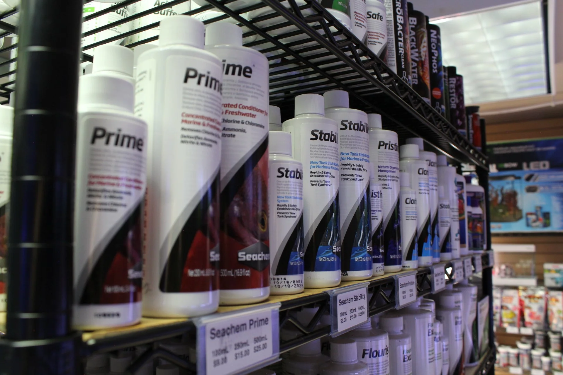 Shelf displaying bottles of Seachem Prime and Stability aquarium additives in a fish store.