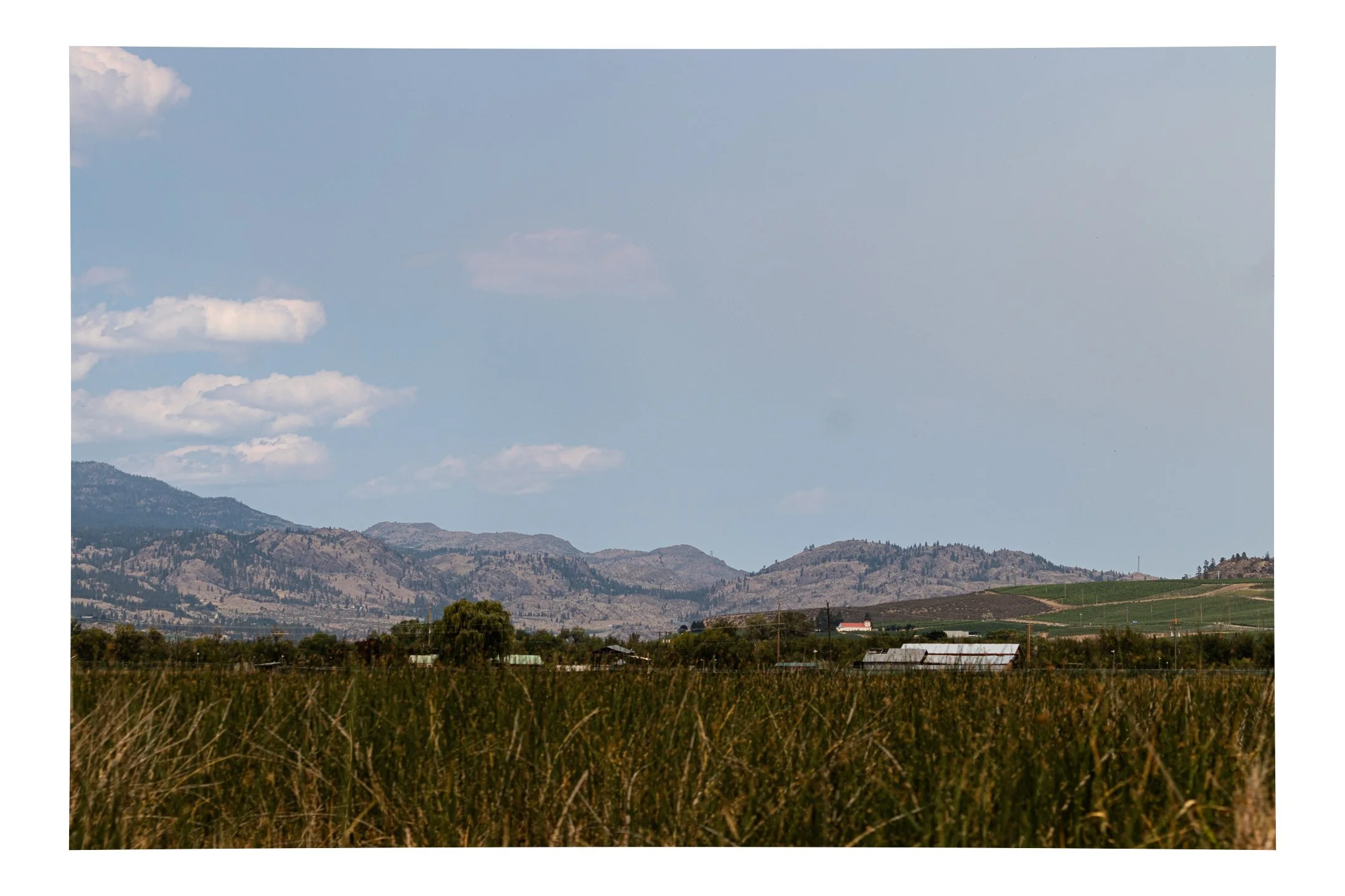 Landscape of mountains, blue sky with scattered clouds, and a rural area with farm buildings and fields in the foreground.