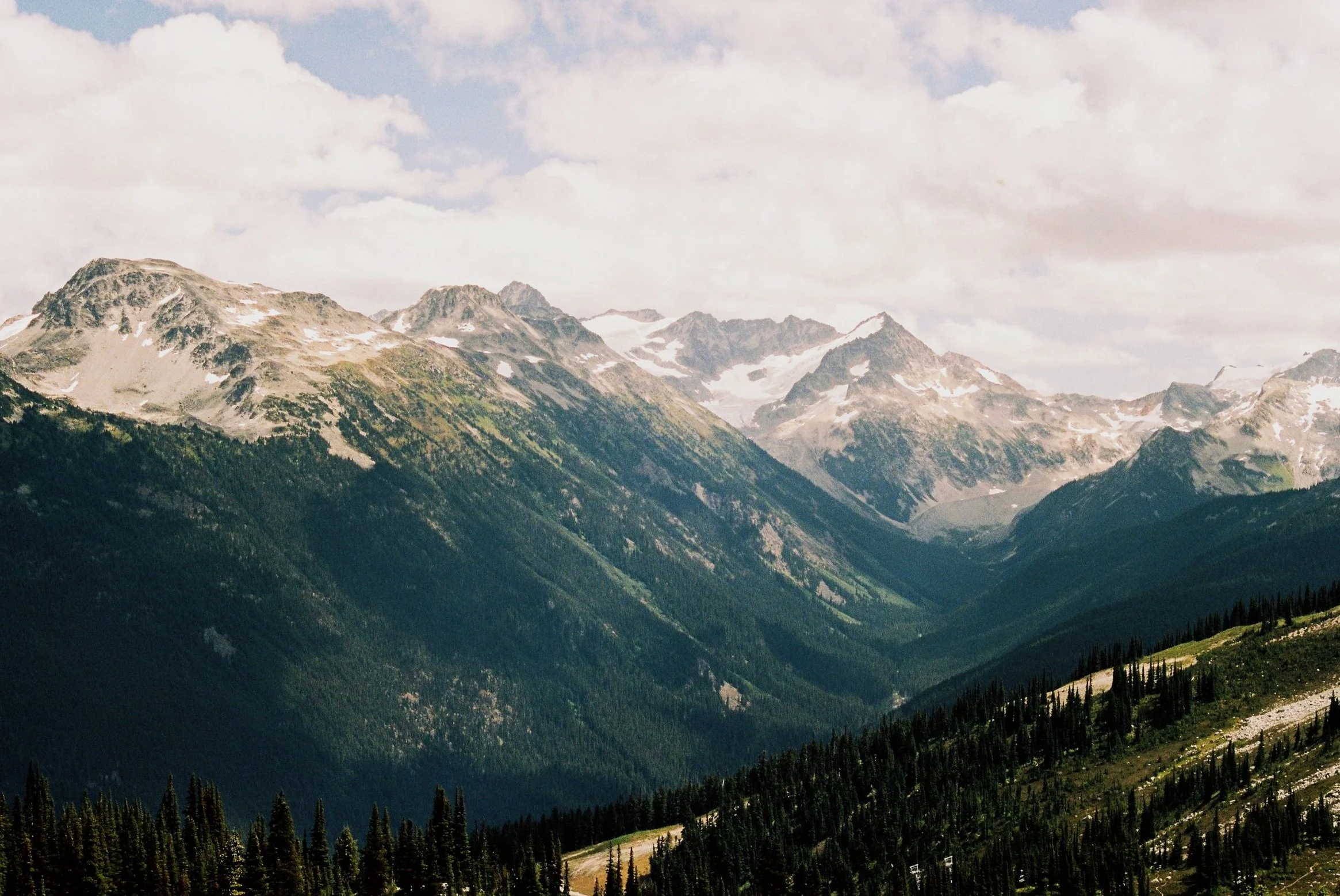 Mountain range with snow patches and green forests, cloudy sky above. Whistler, BC. Shot on Kodak Pro Image 100. 