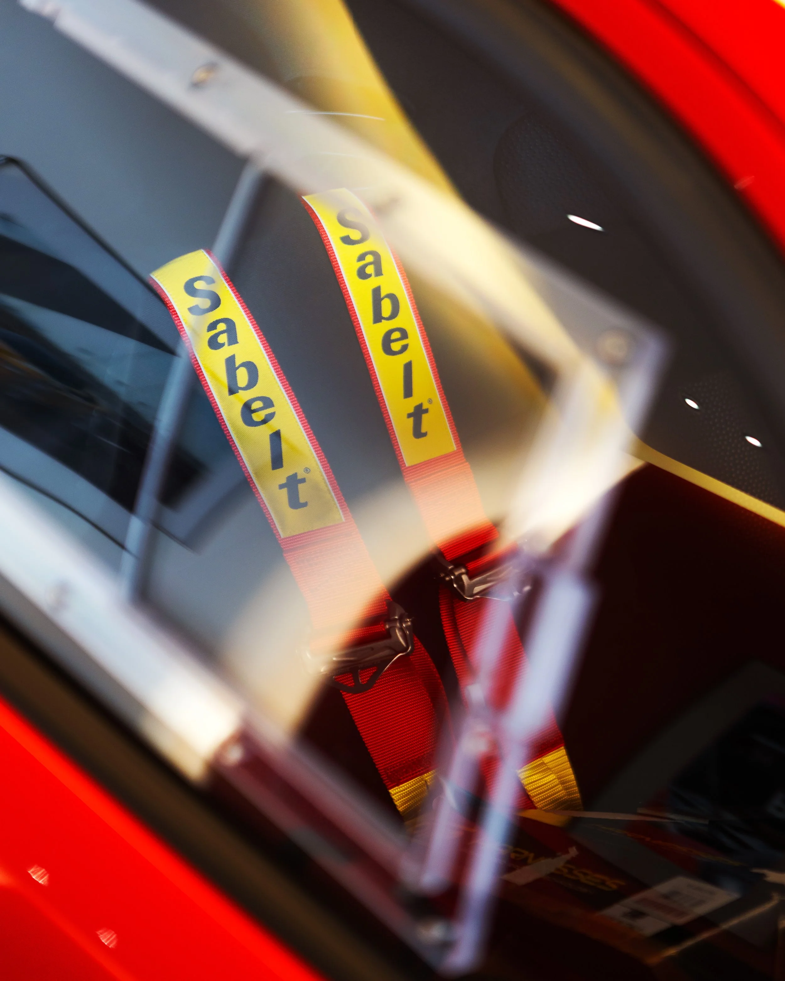 Close-up of bright yellow racing harnesses with 'sabelt' logo inside a red race car, seen through the window.