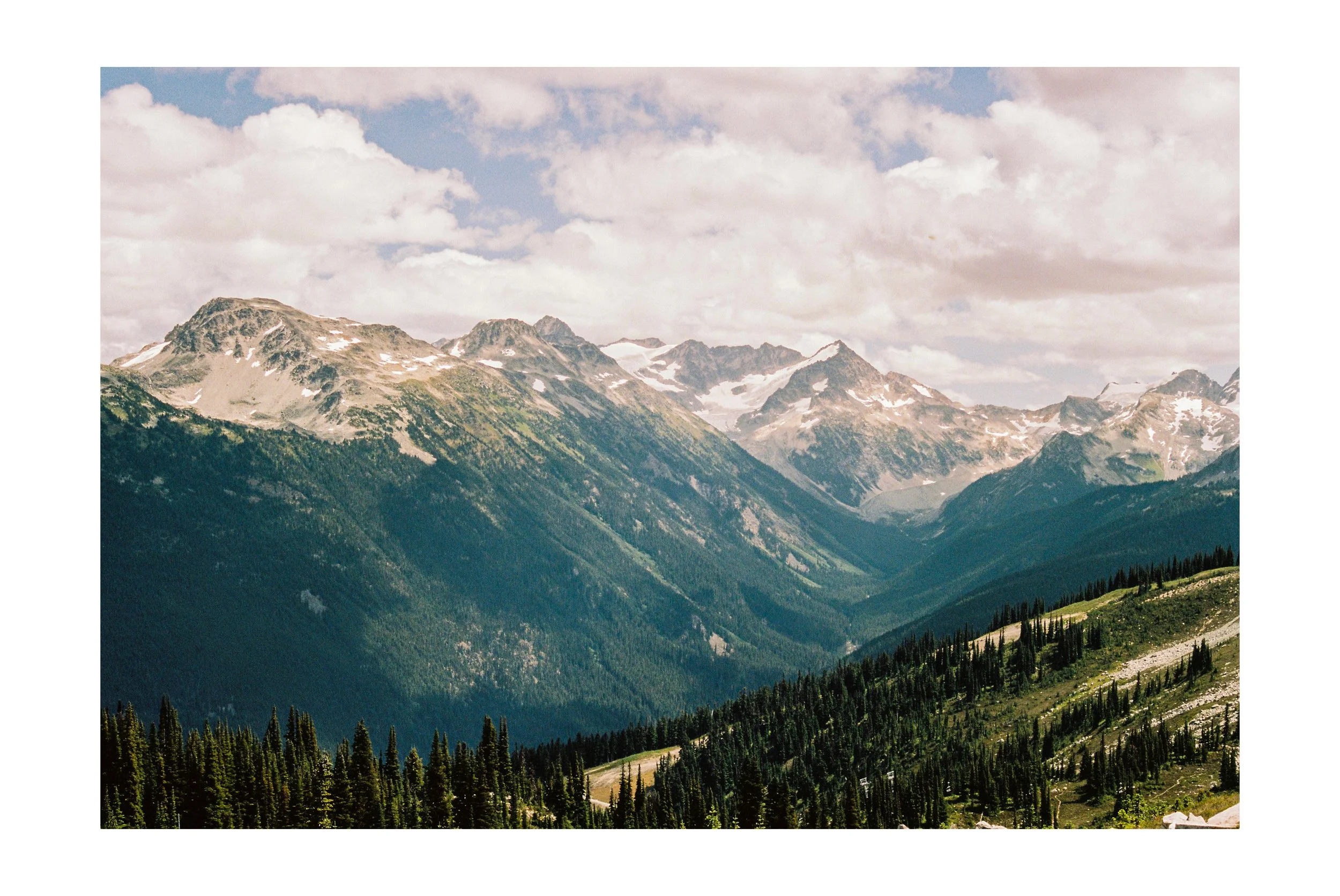 Scenic view of snow-capped mountains with green forested slopes under a partly cloudy sky. Whistler, BC. 