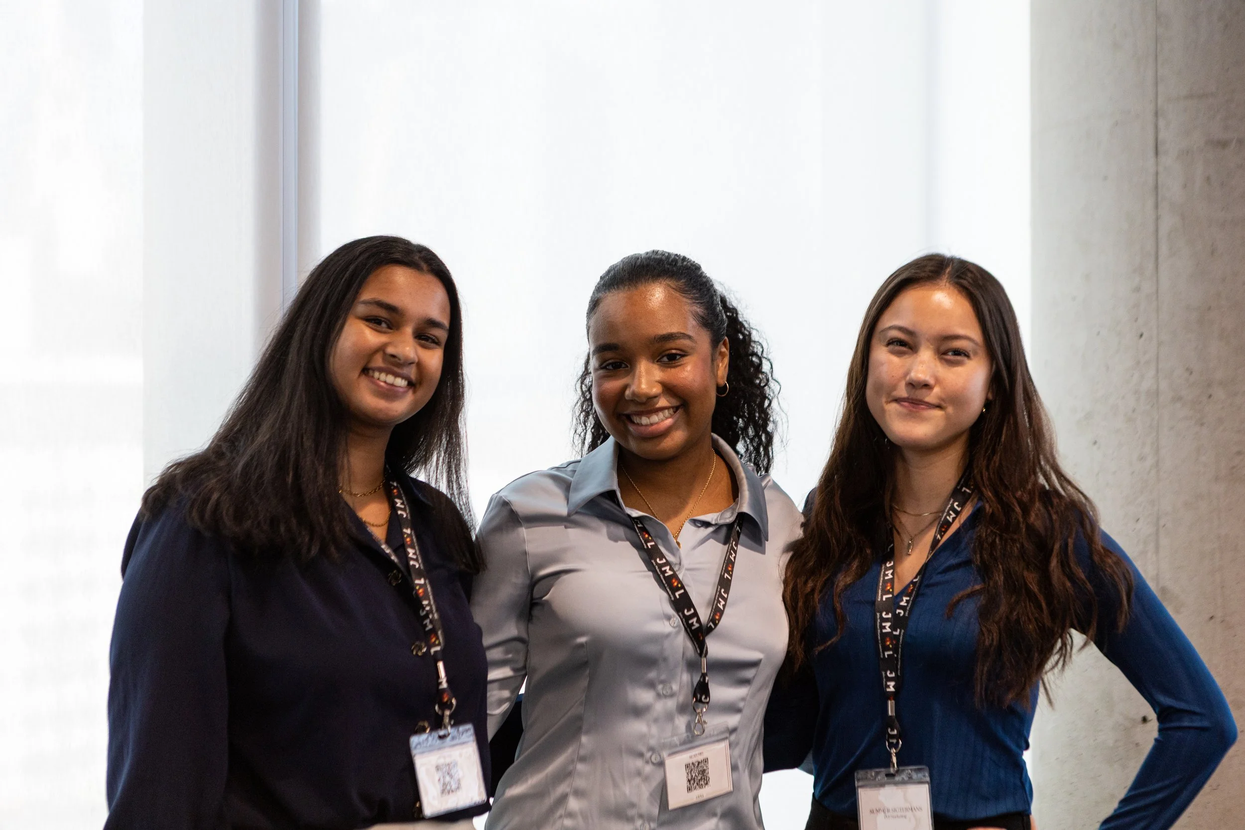 Three Business women smiling and standing close together, wearing conference badges and lanyards.