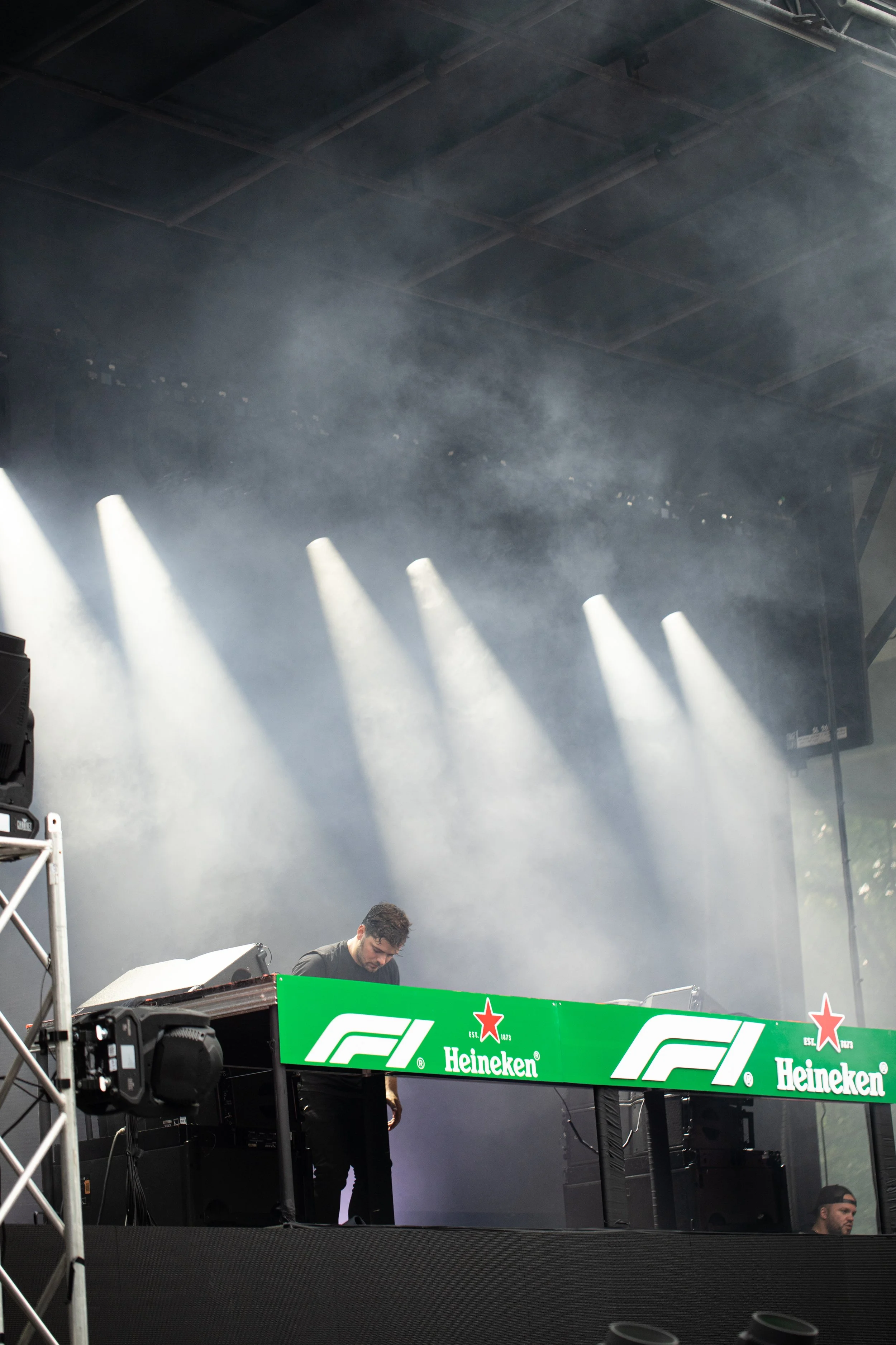 Martin Garrixbperforming on a stage after the Montreal Formula 1 Grand Prix, 2024, with Heineken sponsorship branding, illuminated by bright stage lights with smoke effects, and partially visible people.
