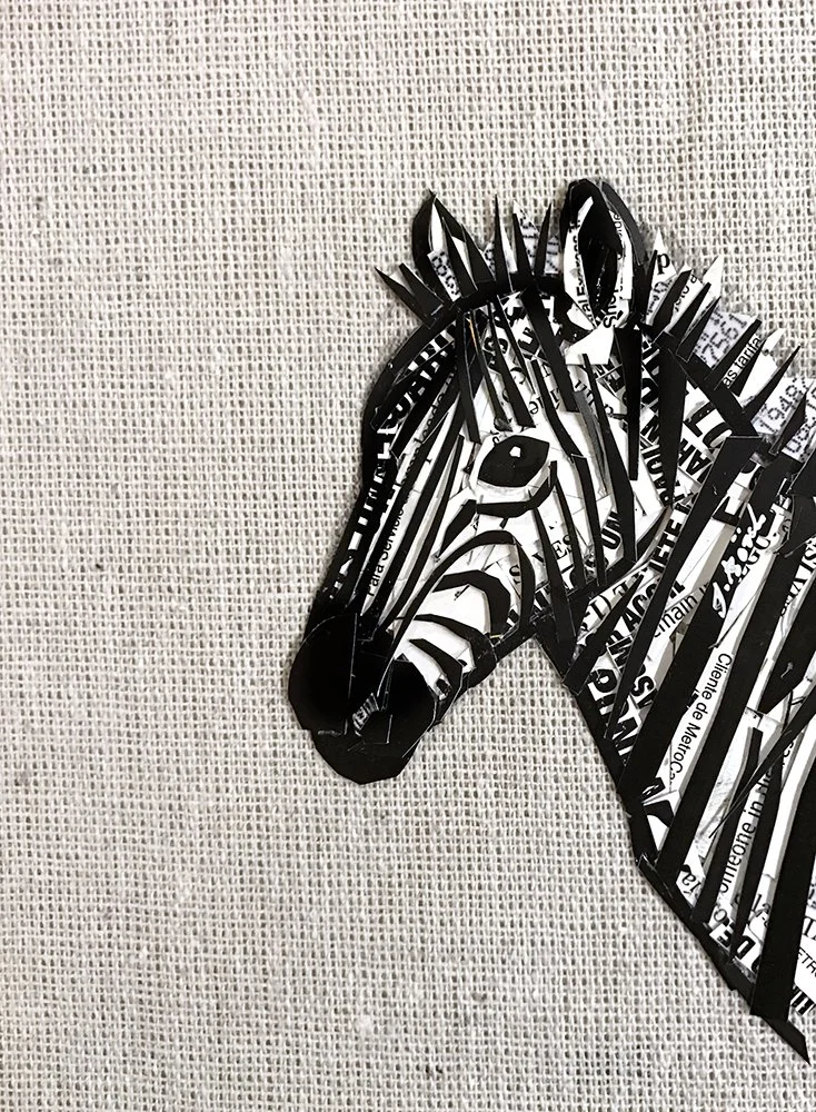 Paper and cardboard sculpture of a zebra's head with black and white stripes, mounted on a textured wall.