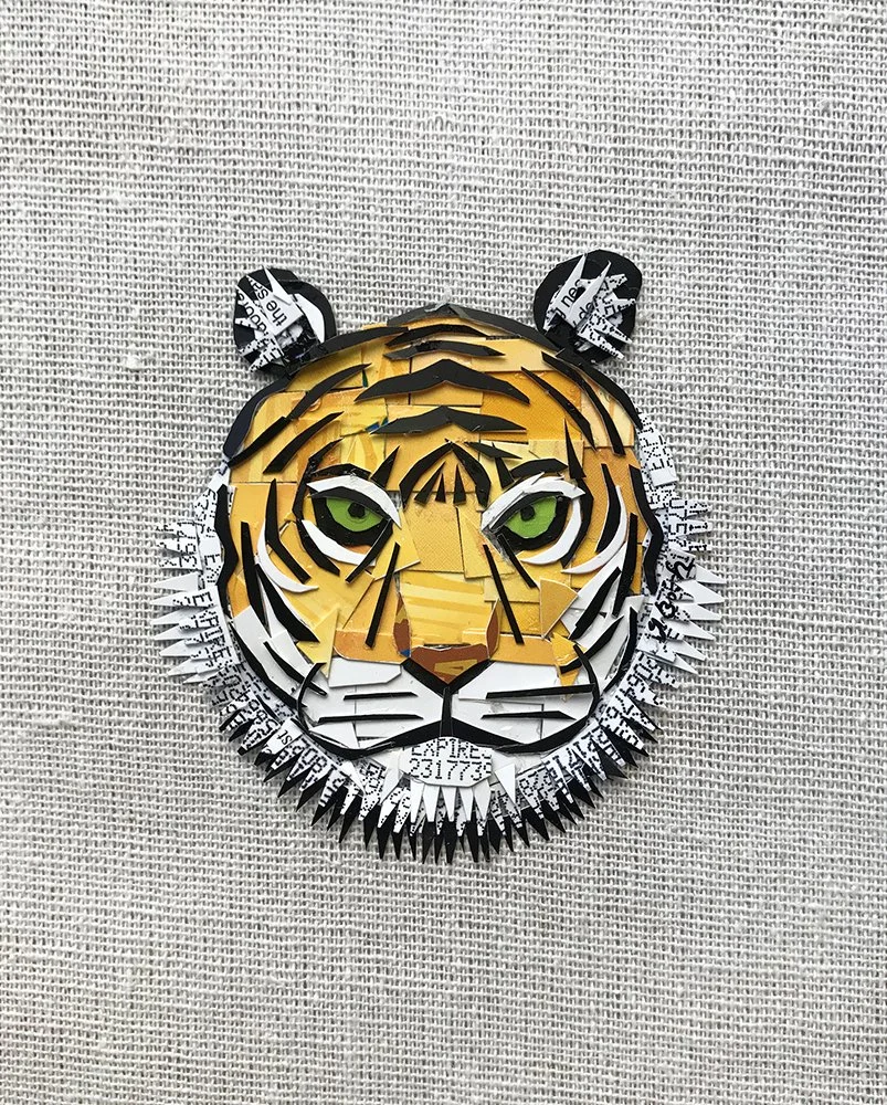 Paper sculpture of a tiger's face on a textured background, featuring green eyes, orange and black striped fur, and white accents.