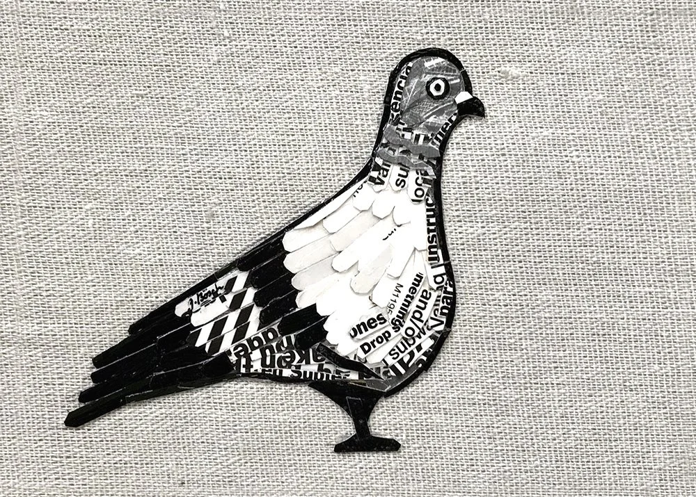 Collage art of a bird created from black and white paper cutouts on fabric background.