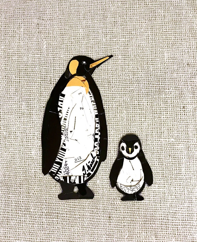 Paper cutout pair of penguins, one adult and one chick, set against a textured fabric background.