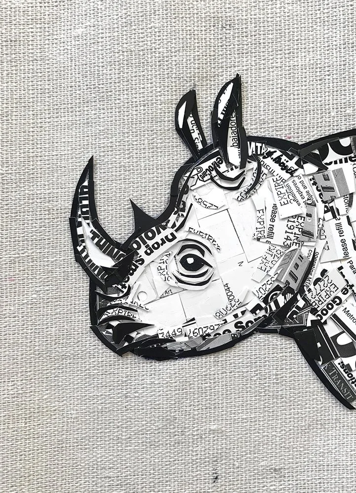 A paper collage of a cartoon unicorn face with a white mane and horn, created from cut-out magazine and newspaper pieces, on a light textured background.