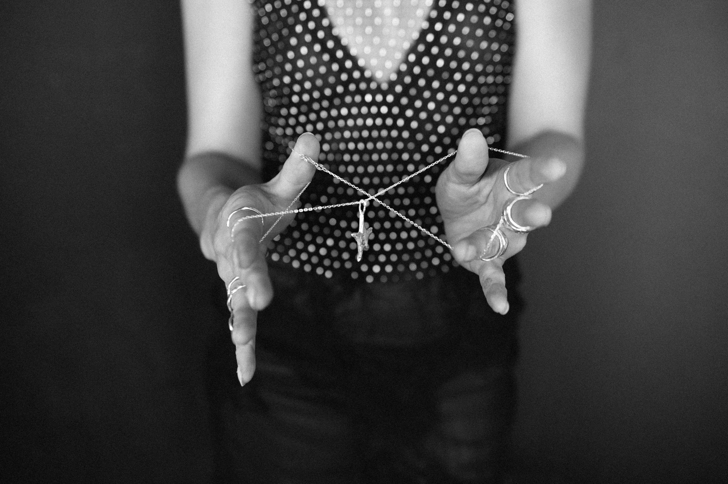 Person holding a necklace with a cross pendant, wearing multiple rings, in a polka dot top, in black and white.