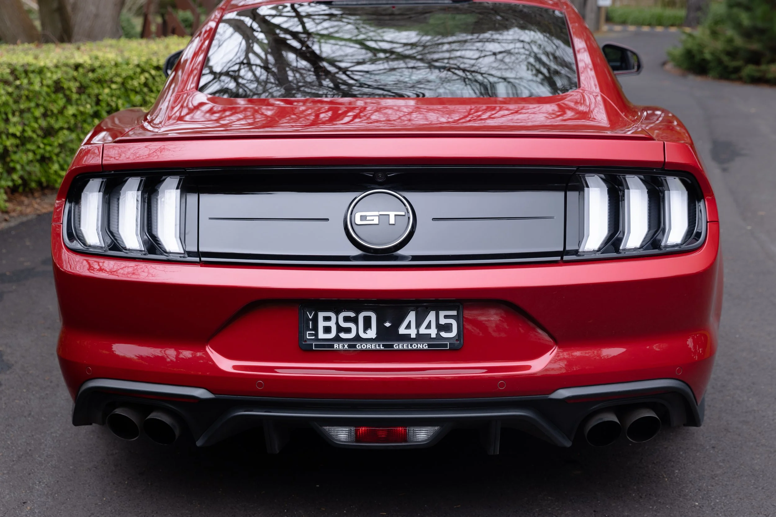 Rear view of a red Ford Mustang GT with black taillight panel, black exhaust pipes, and a Vic license plate reading 'BSQ 445'.