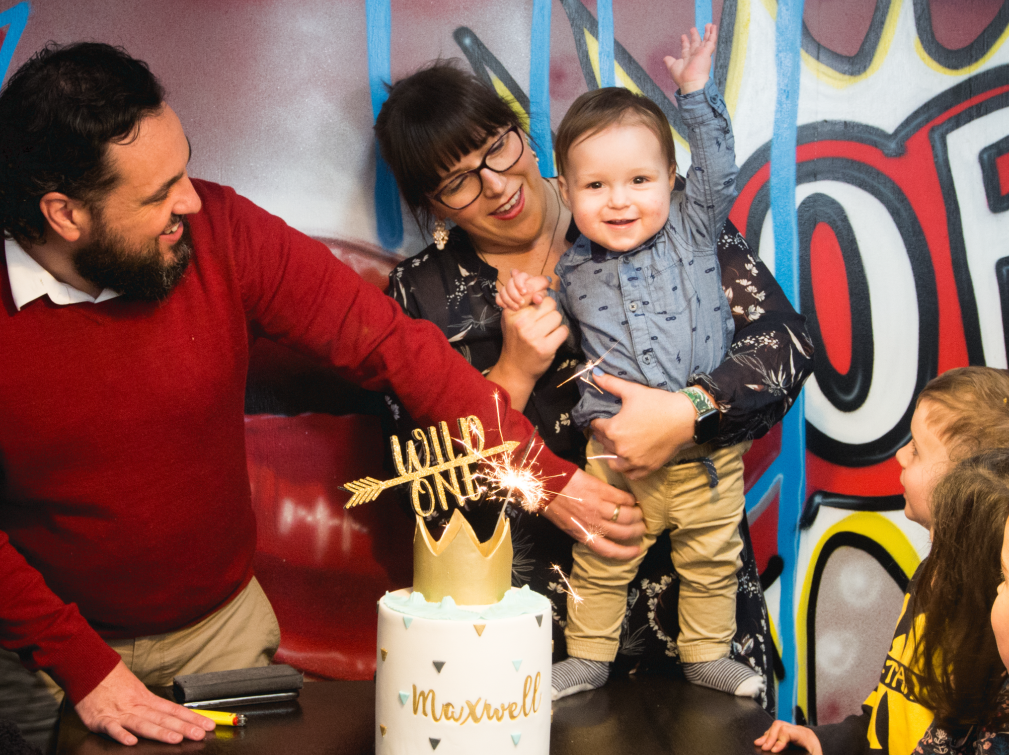 Young family celebrating first birthday. Mother, father and young child with a birthday cake in front.