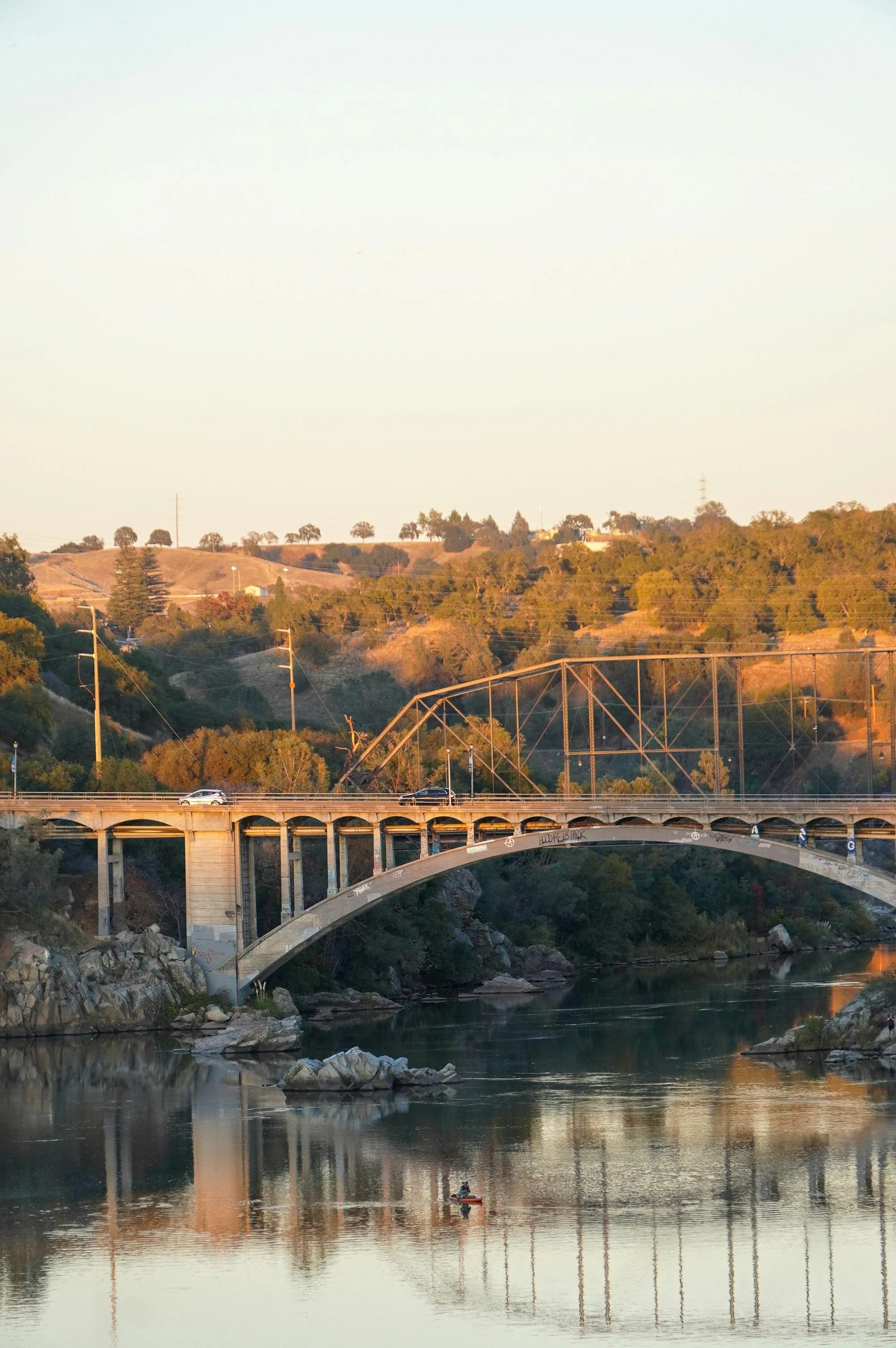 Scenic view of a bridge over a river with hills and trees in the background during sunset.