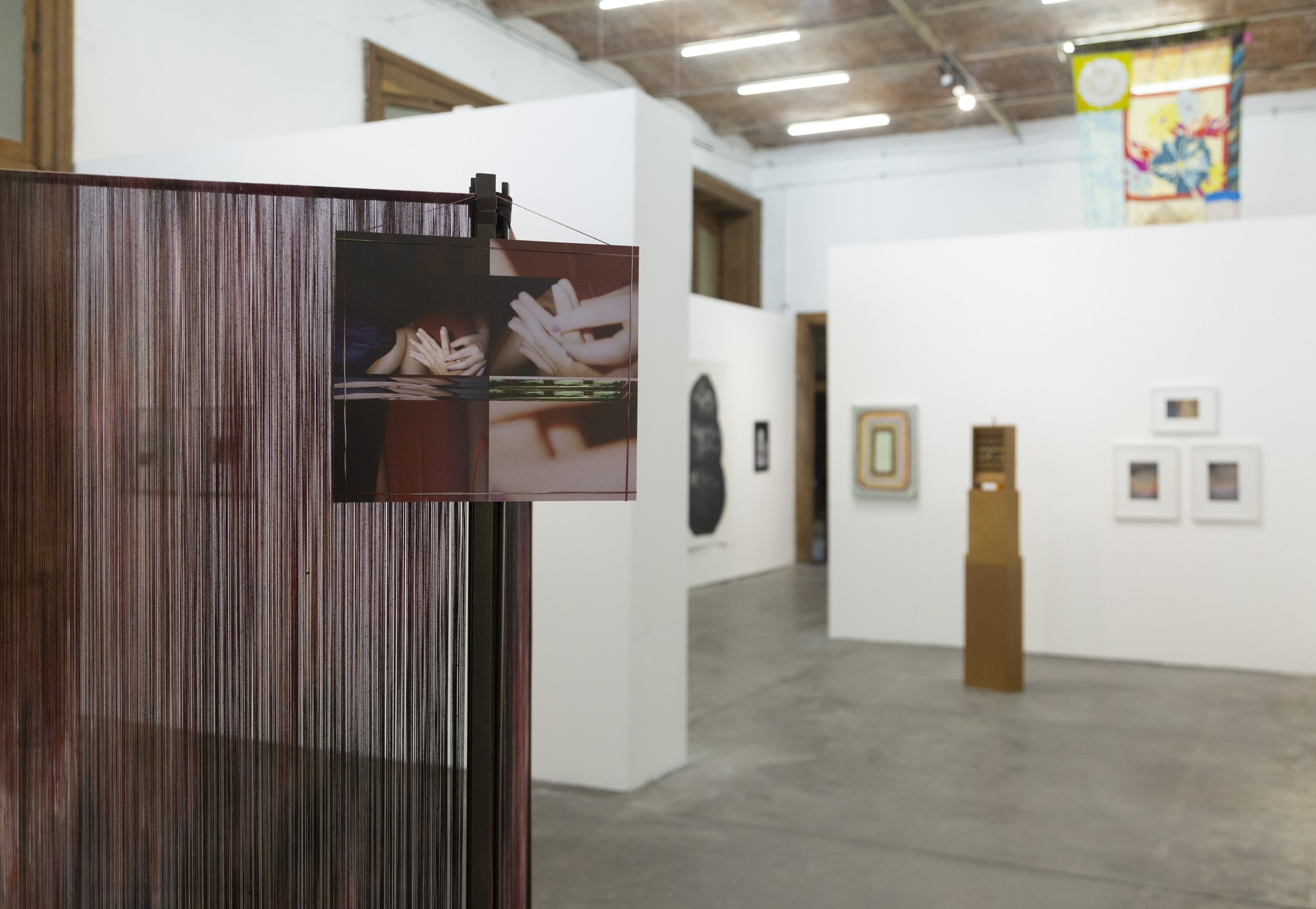 Art gallery with artworks on white walls, wooden ceiling, and a red textured display stand in the foreground.