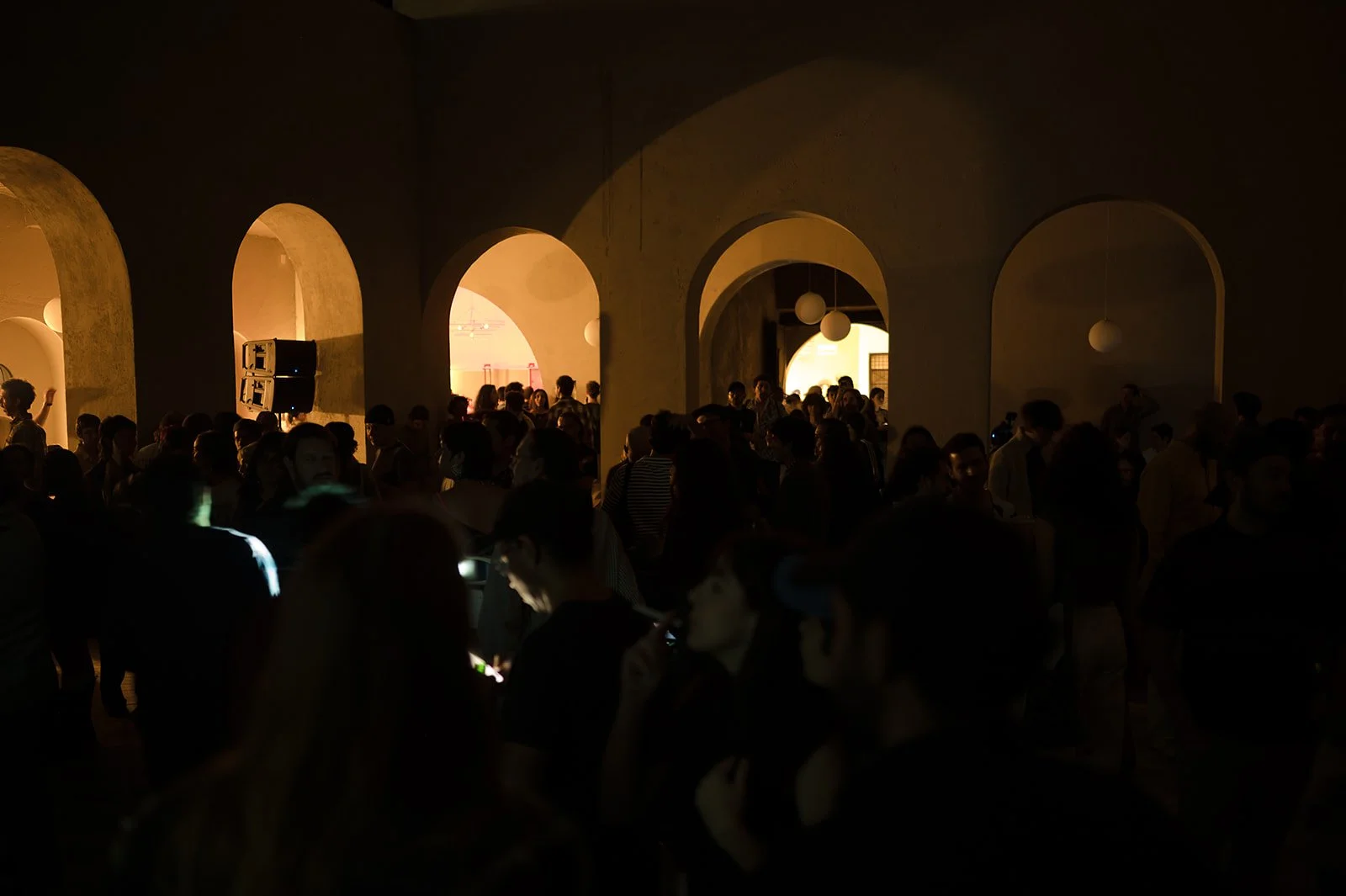 Crowd of people in a dimly lit room with arched doorways and warm lighting.