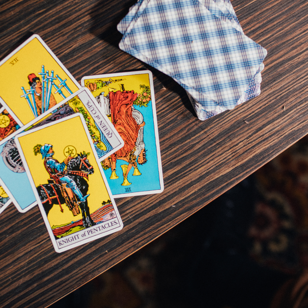 A scattered pile of tarot cards on a wooden surface with a deck of face-down tarot cards nearby.