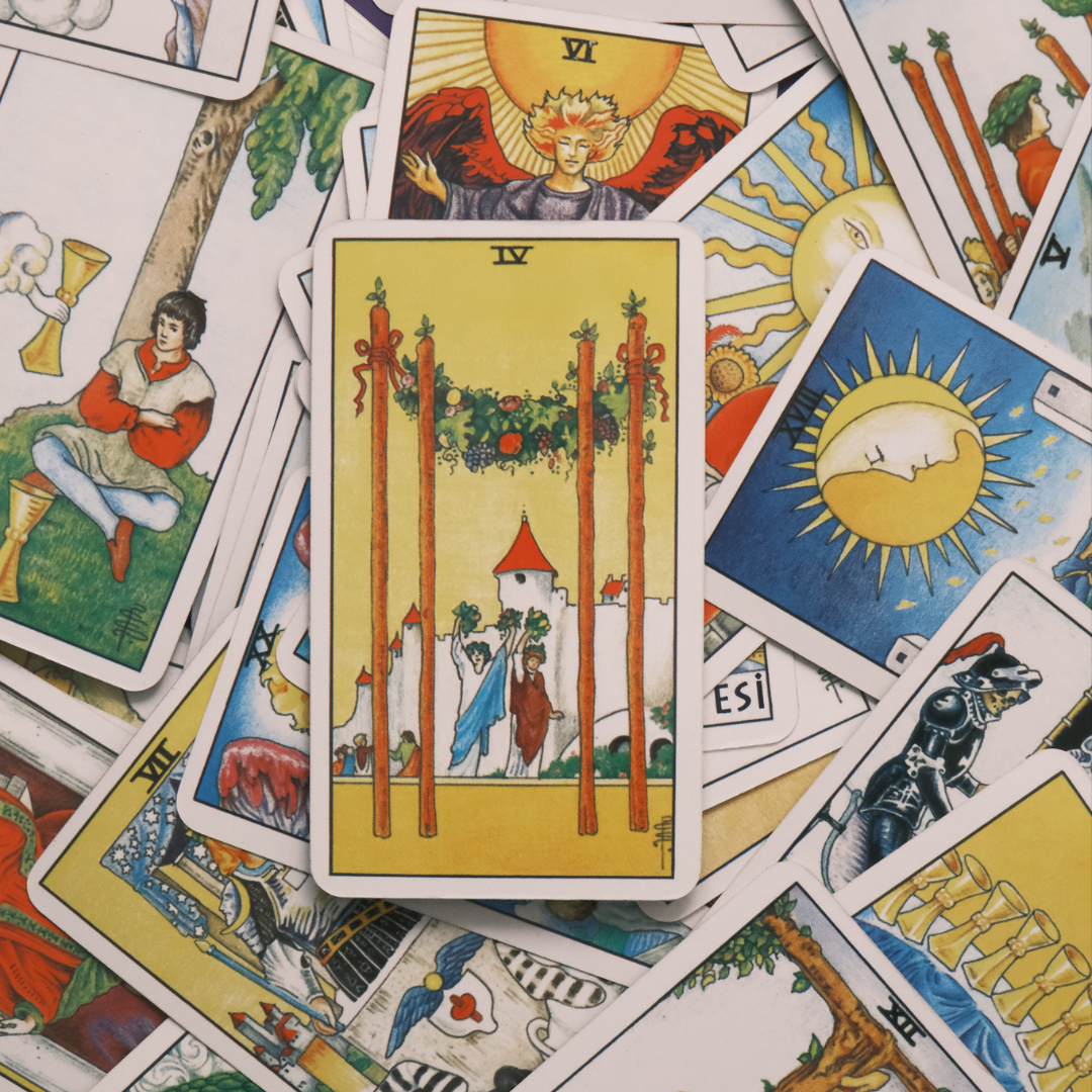 Various tarot cards laid out, with the Four of Wands card prominently displayed in the center showing two figures celebrating under a decorated arch.