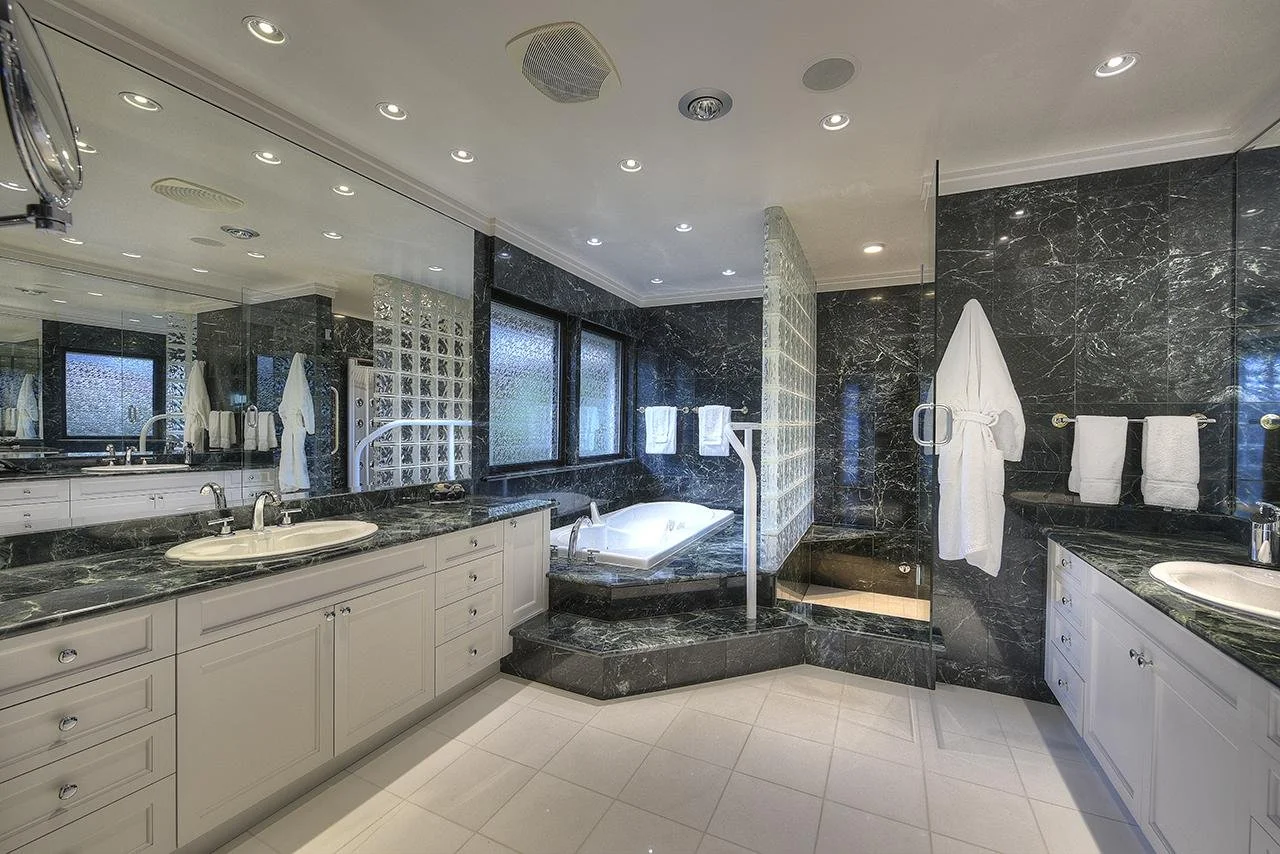 A luxurious bathroom with black marble countertops and walls, white cabinetry, a bathtub, a shower, a large mirror, and towels hanging on towel racks.