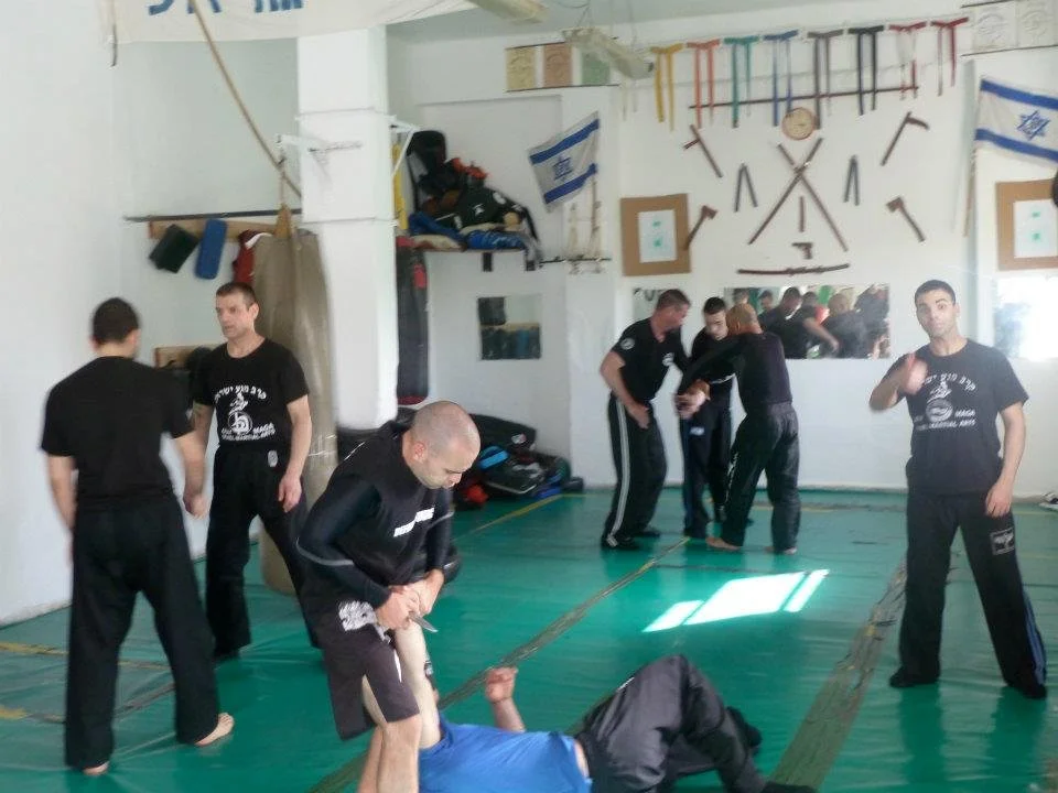 People practicing martial arts in a dojo with equipment on the walls and floor mats.