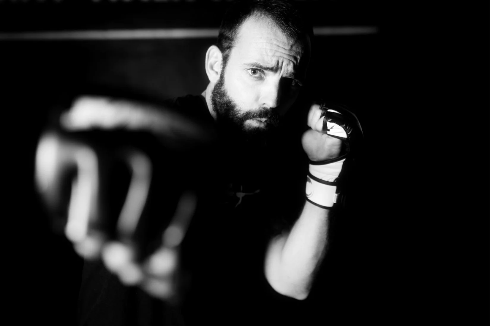 Black and white portrait of a bald man with a beard, wearing a light-colored suit and white shirt, standing against a plain background.