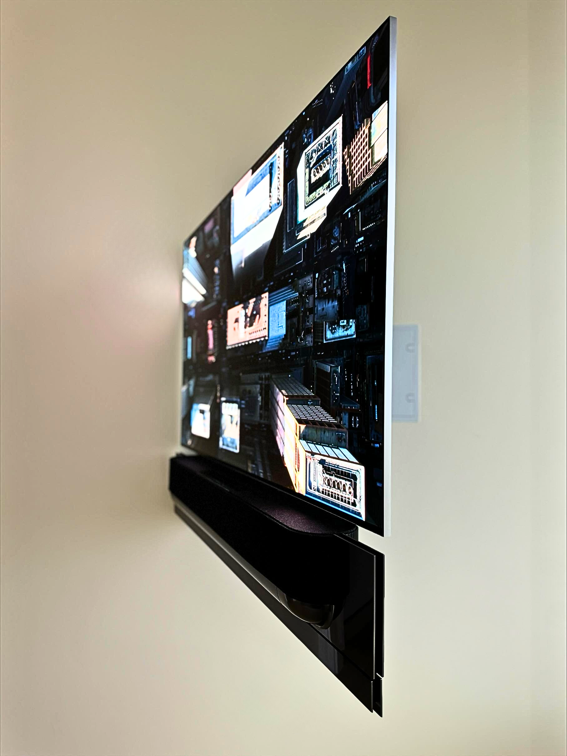 Close-up of a flat-screen TV mounted on a beige wall, displaying a collage of various digital images and screens.