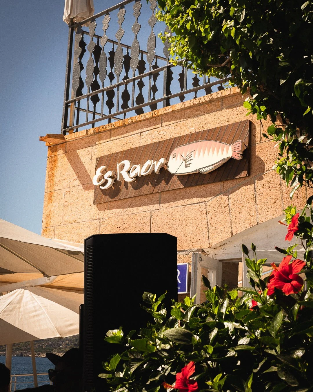 Letrero de madera con la marca 'Es Raor' y la ilustración de un pescado raor, en la pared de piedra caliza de la terraza del Restaurante Es Raor en Sant Elm, Andratx, Mallorca.